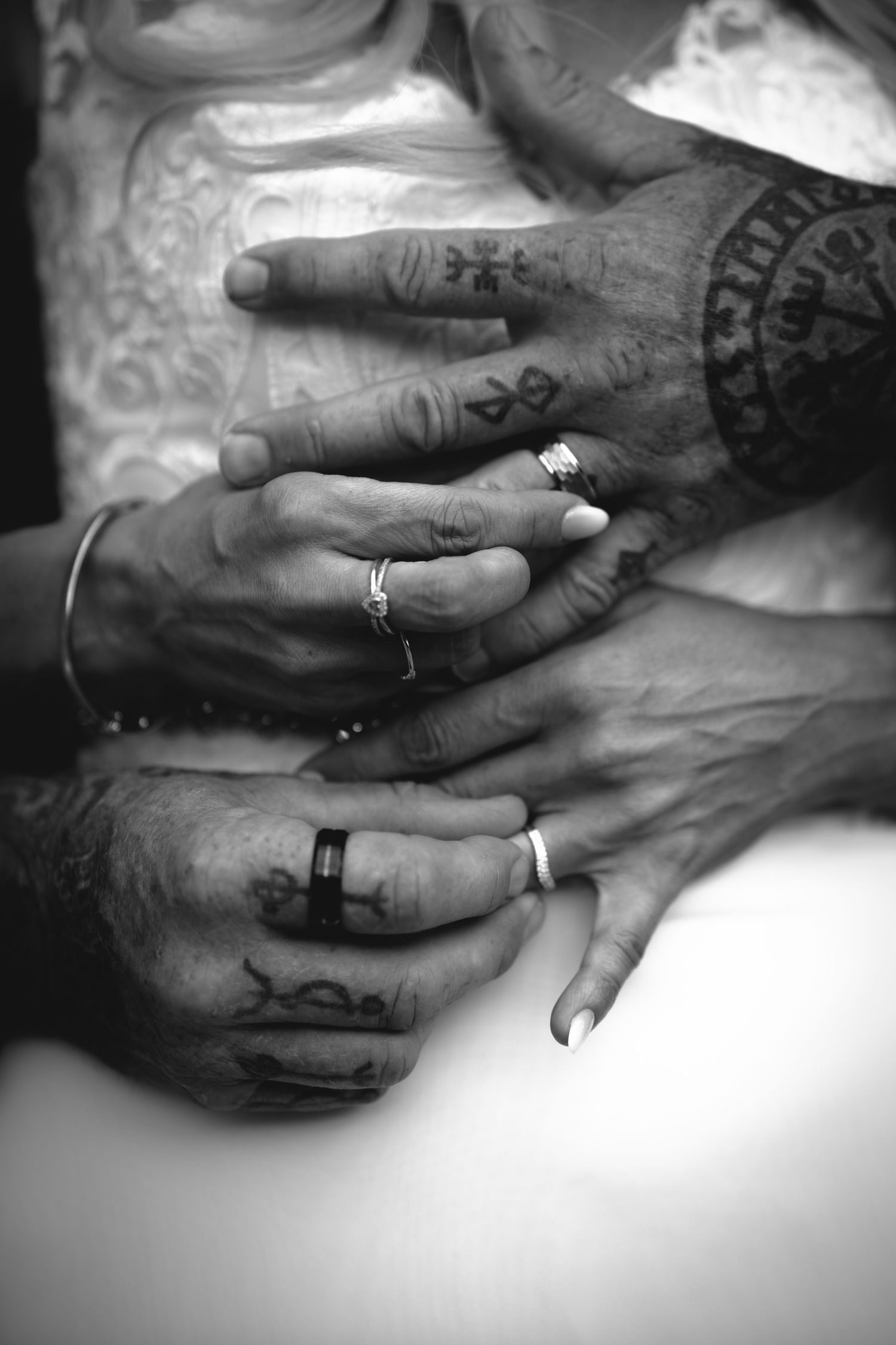 Black and white close-up of hands with tattoos and wedding rings intertwined.