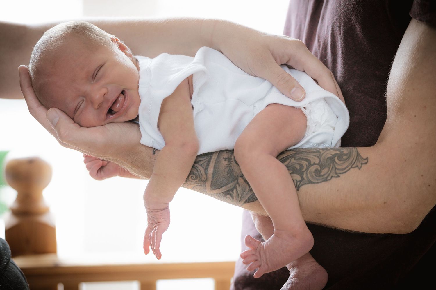 A joyful baby in white clothing being held up and laughing.