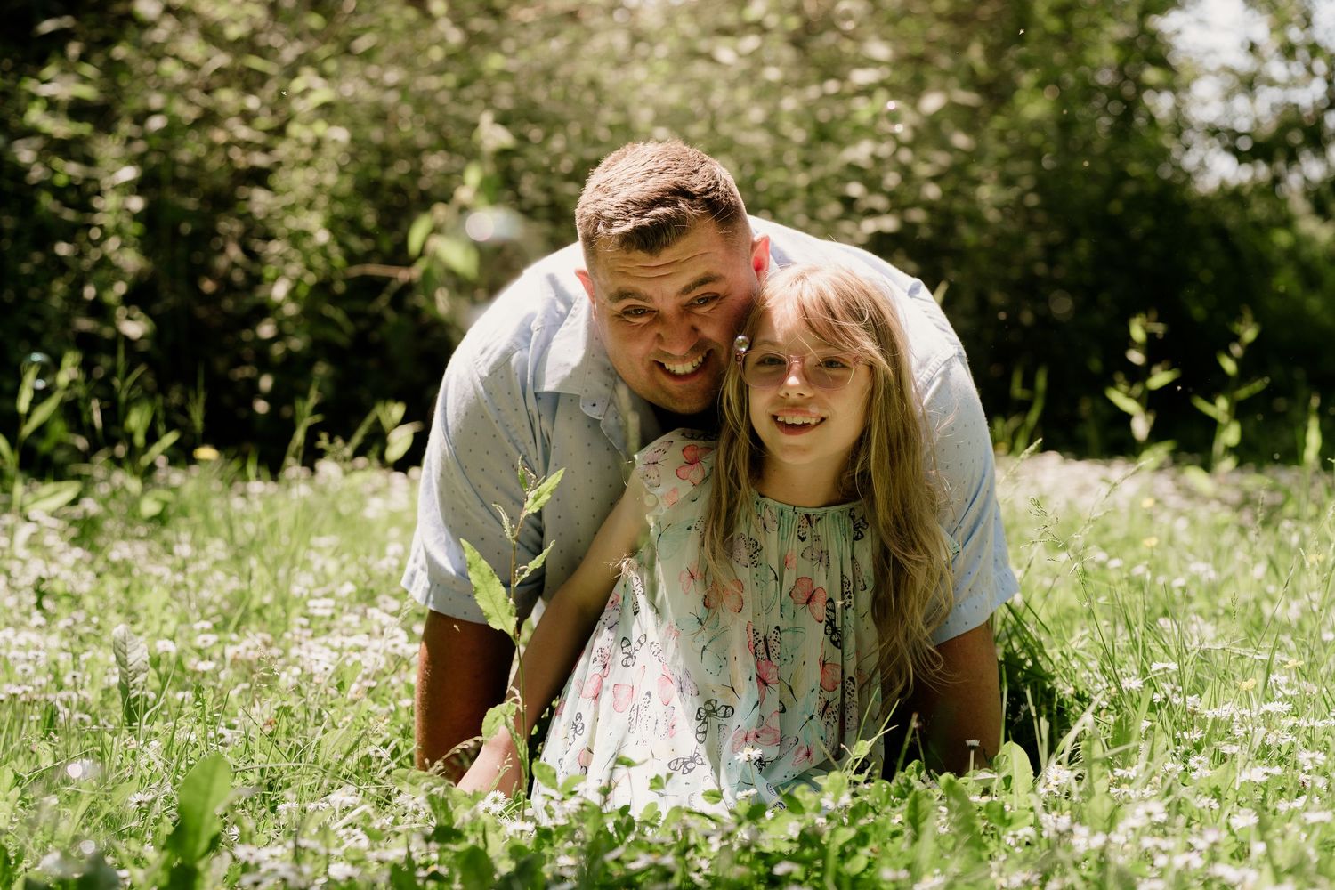Two people laying in a meadow of white wildflowers on a sunny day.