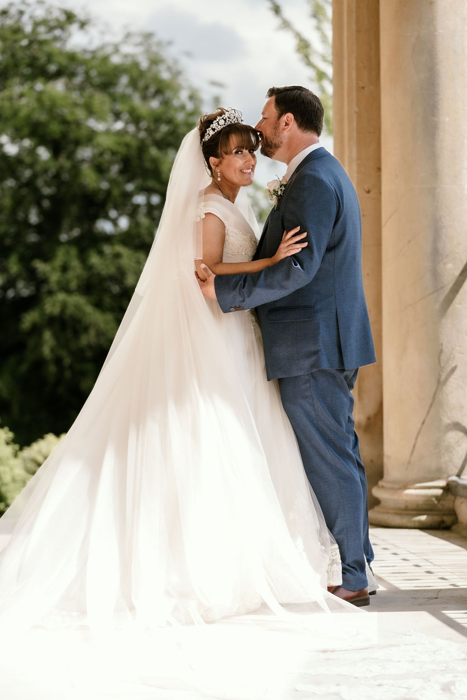 A romantic wedding portrait of a couple embracing by a classical column.