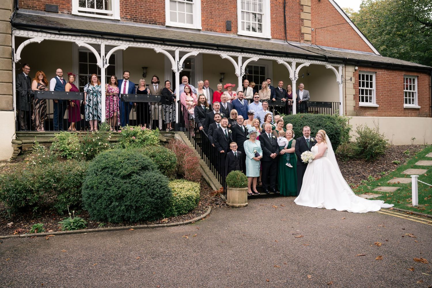 Large wedding party gathered on the steps of a brick building with ornate white porch columns.