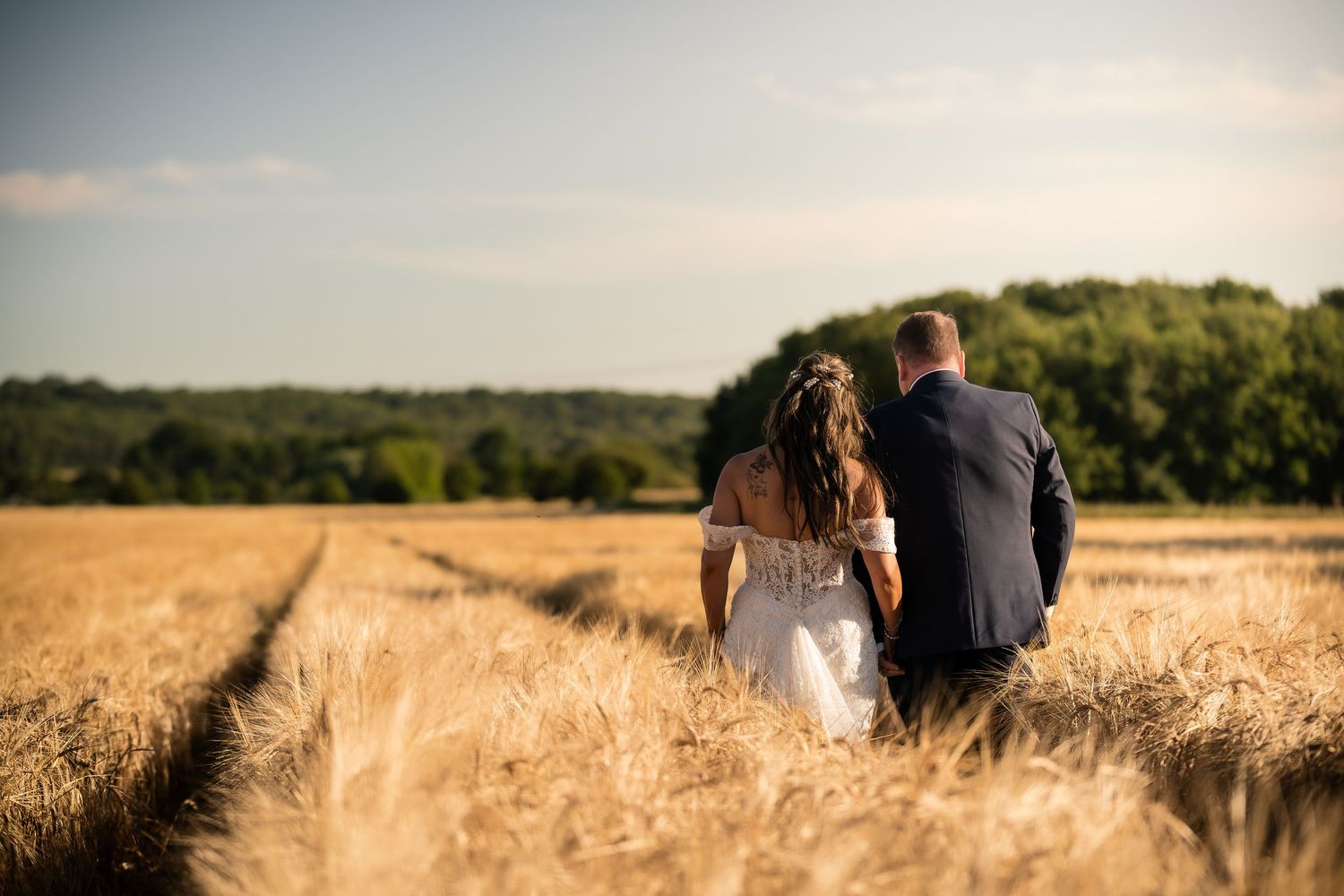 A couple walks through a golden wheat field on their wedding day at sunset.