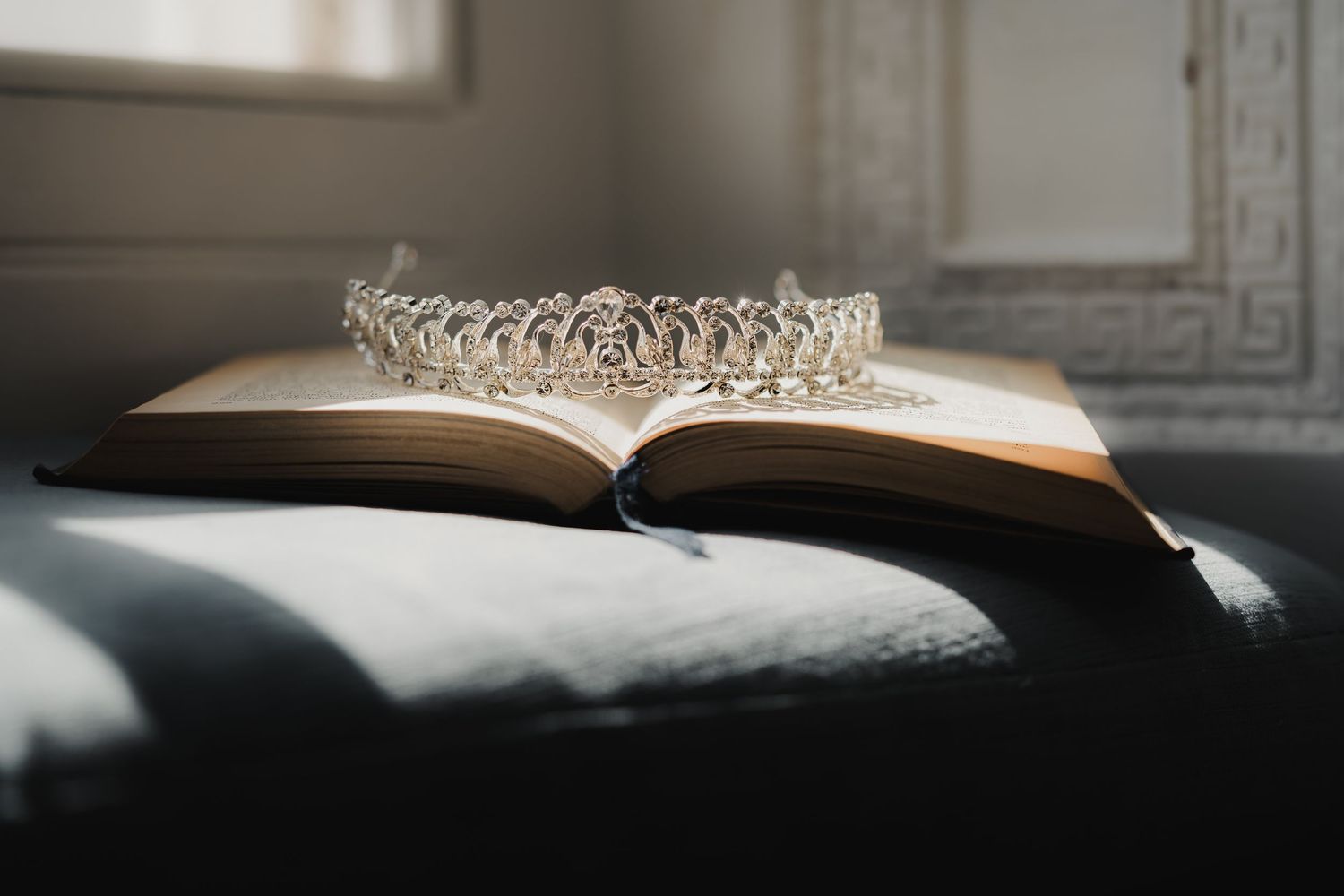 Artistic close-up of an open book and delicate crystal tiara in dramatic lighting.