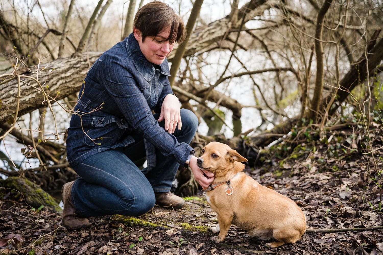Person kneeling beside a small tan dog on a forest trail.