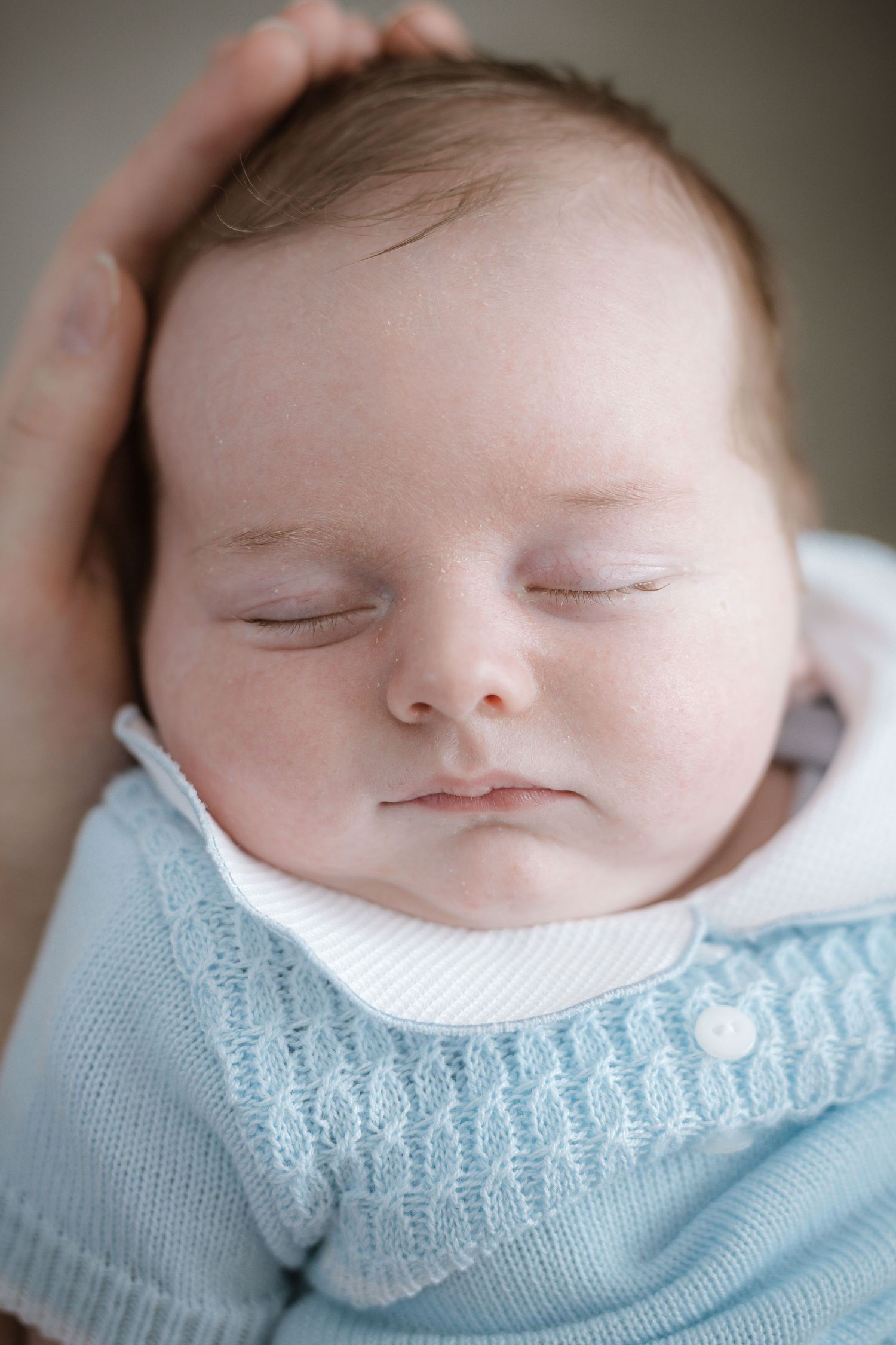 Sleeping baby wearing light blue knit sweater in soft focus portrait.