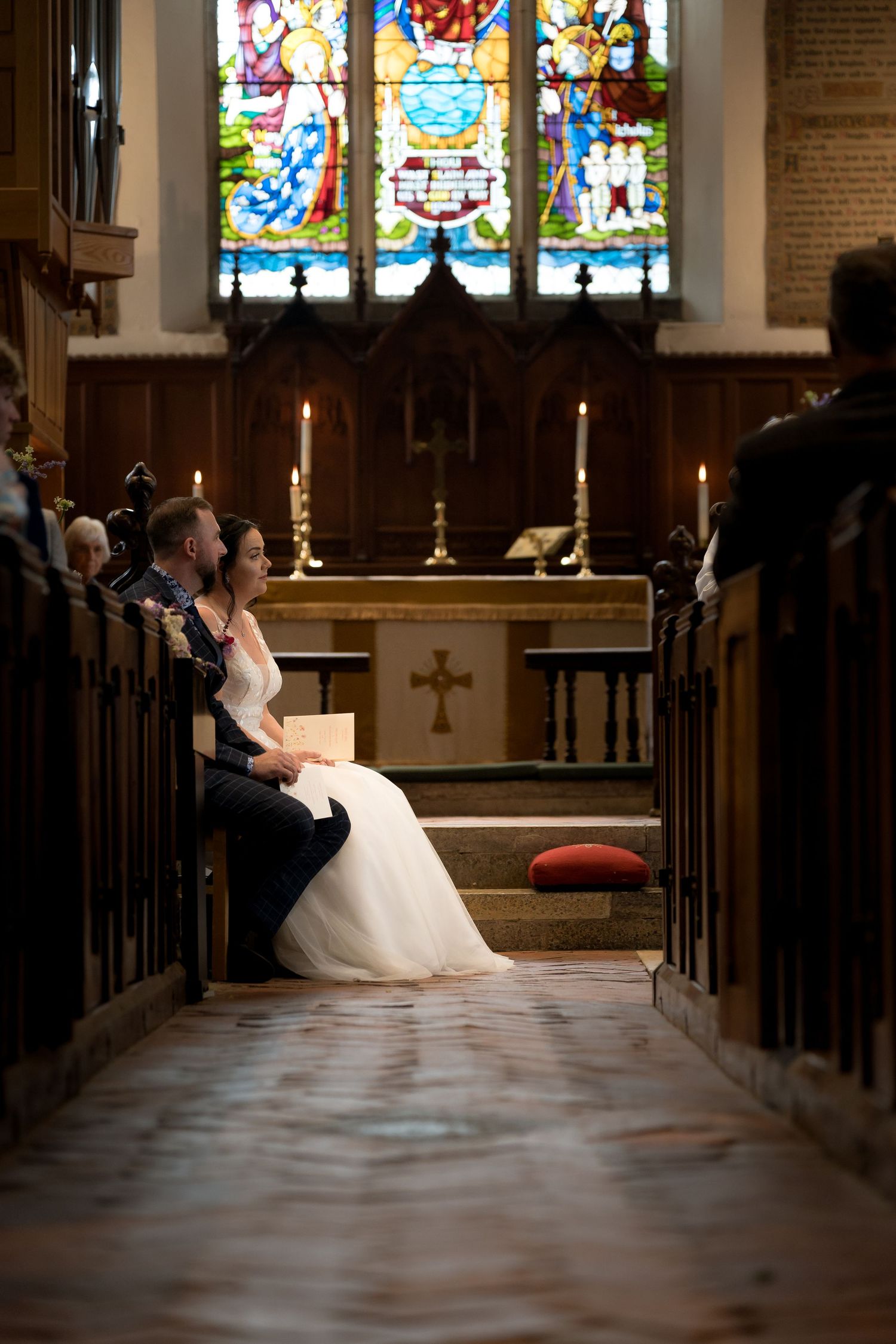 A wedding ceremony moment in a church with stained glass windows and wooden pews.