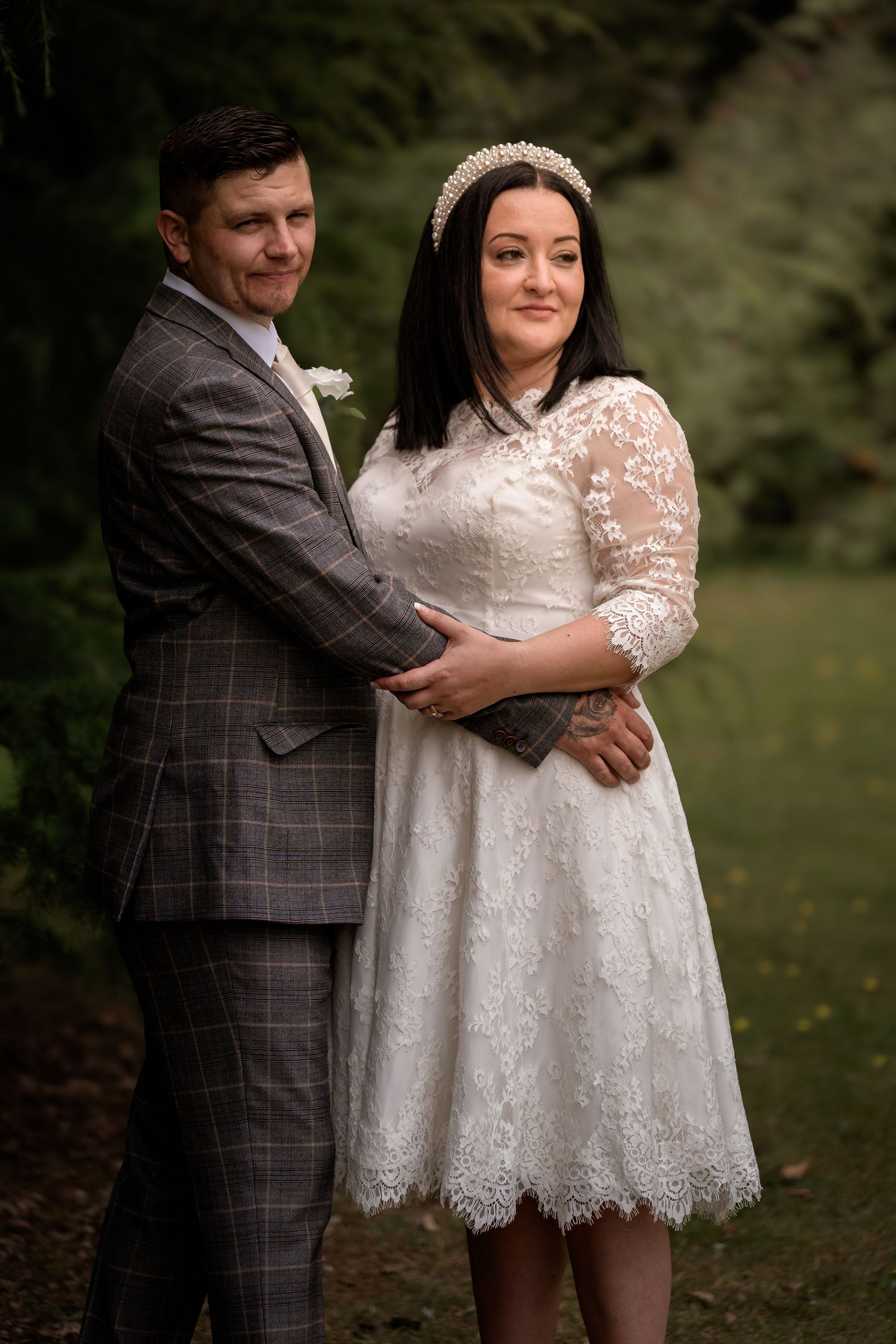 Wedding portrait in woodland setting with couple in lace dress and checked suit.
