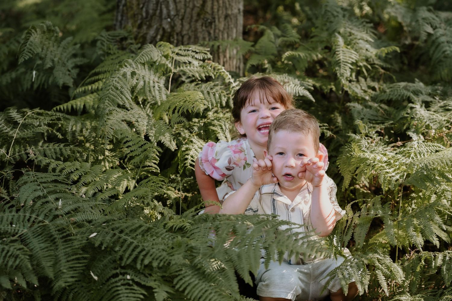 Playful moment captured with children peeking through lush fern leaves in the forest.