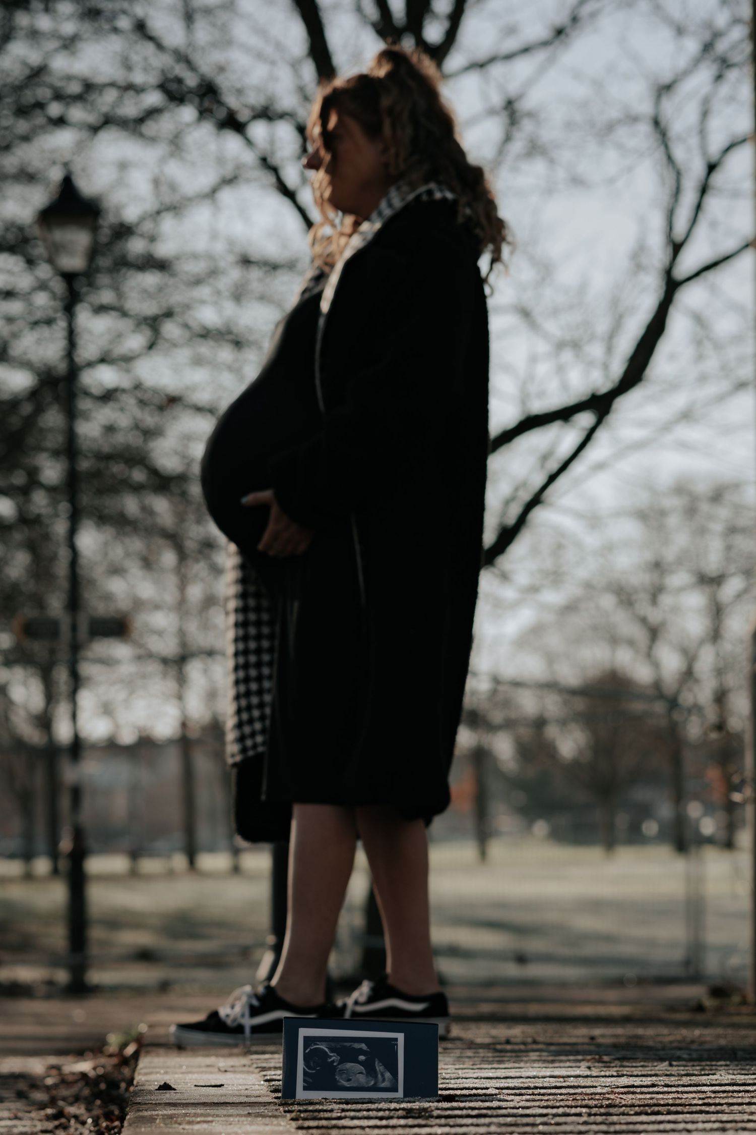 Silhouette of pregnant woman on walkway with ultrasound photo at feet.