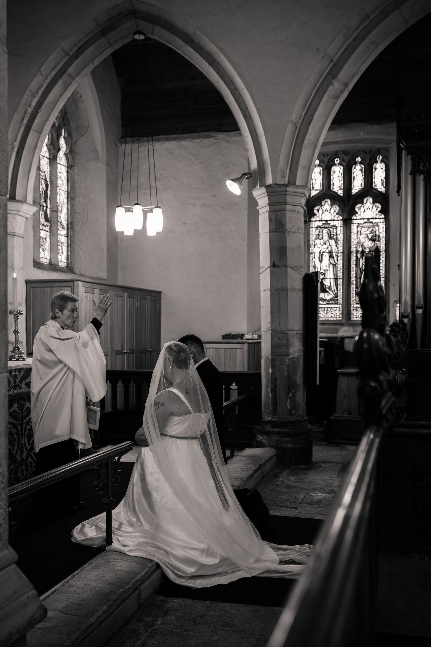 Black and white photo of wedding ceremony in historic church with Gothic arched windows and stained glass.