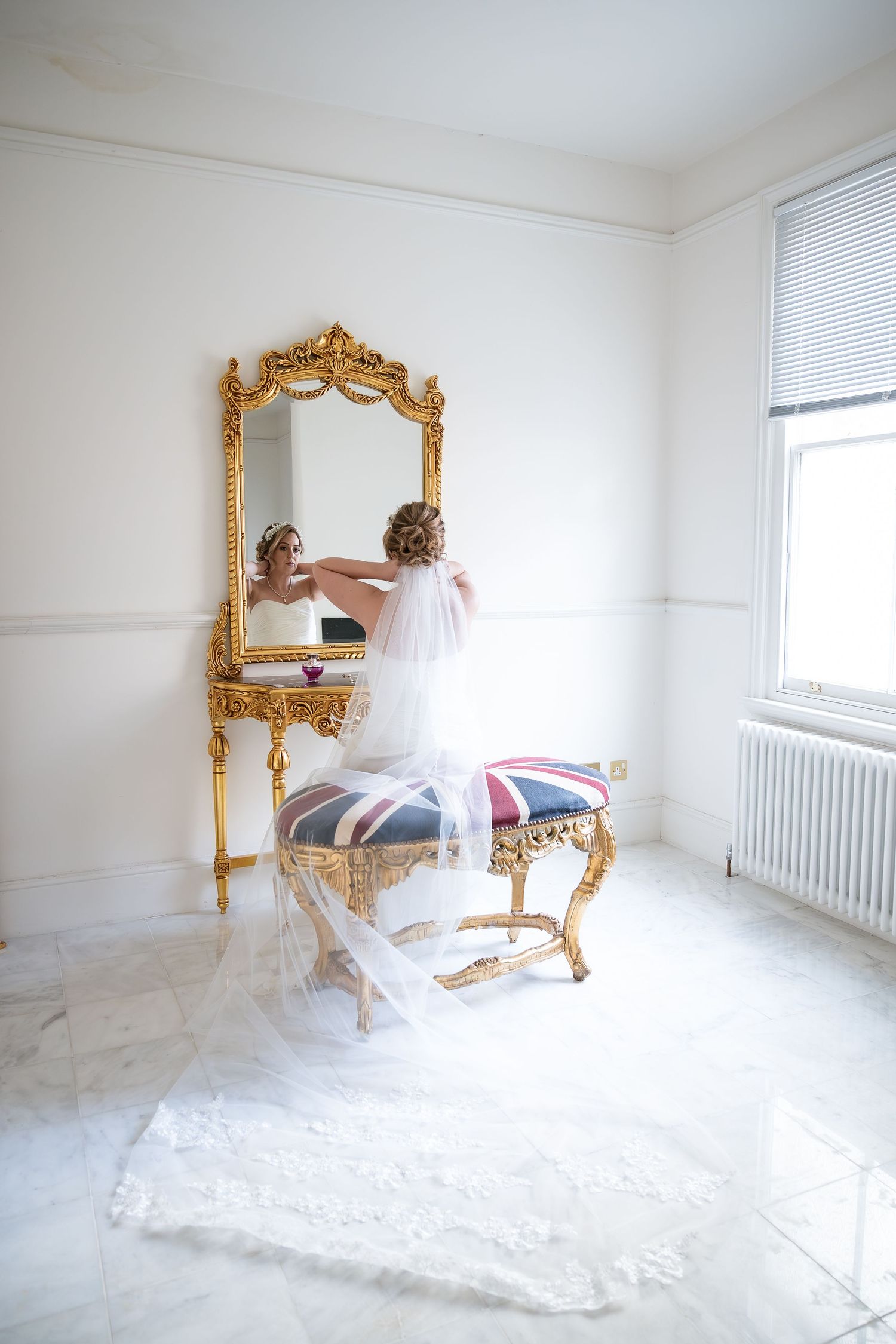 Elegant gold ornate mirror and chair with Union Jack cushion in bright white room.
