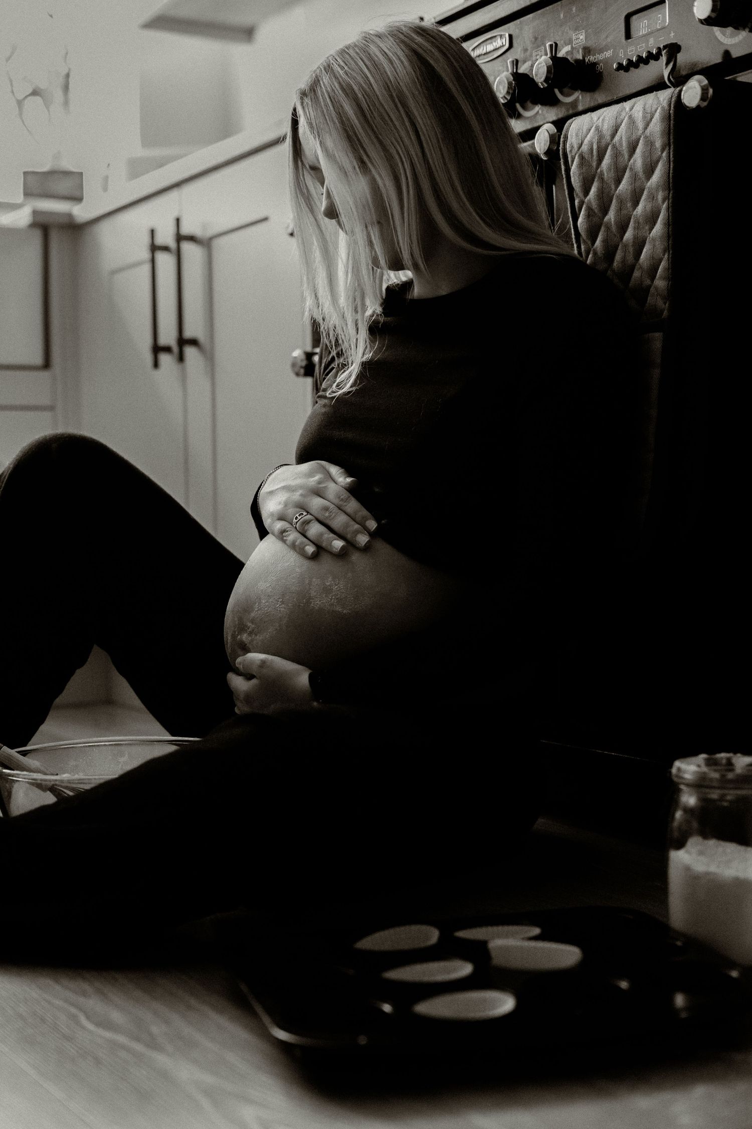 Black and white photo of expectant mother sitting on floor holding her belly.