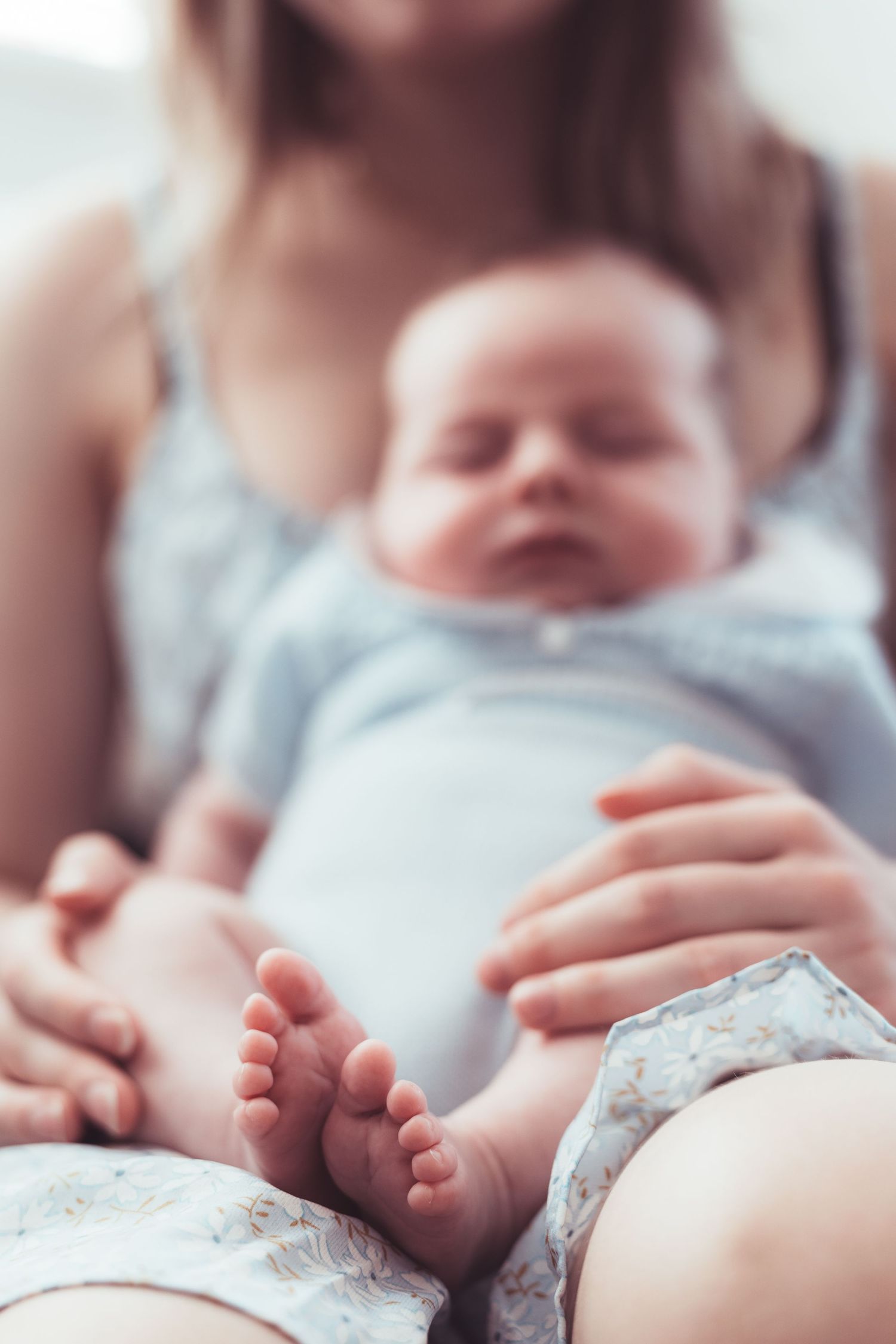 Sleeping baby in blue outfit rests on caregiver's lap with tiny feet visible.