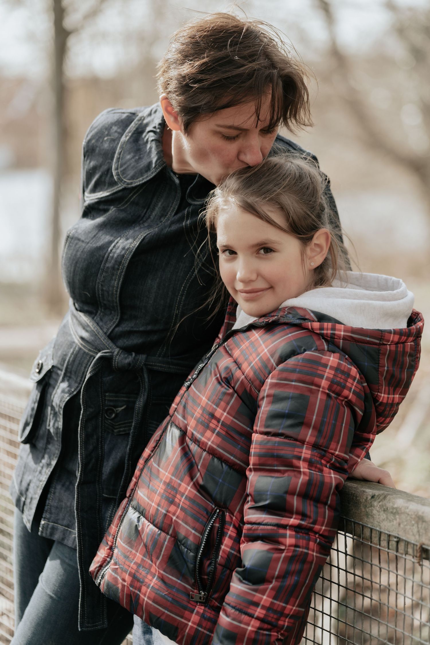 Two people in winter coats share a tender moment while leaning on a railing outdoors.
