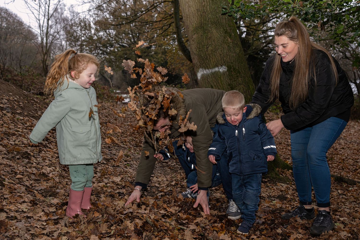 Family playing together in fallen autumn leaves on a forest floor.