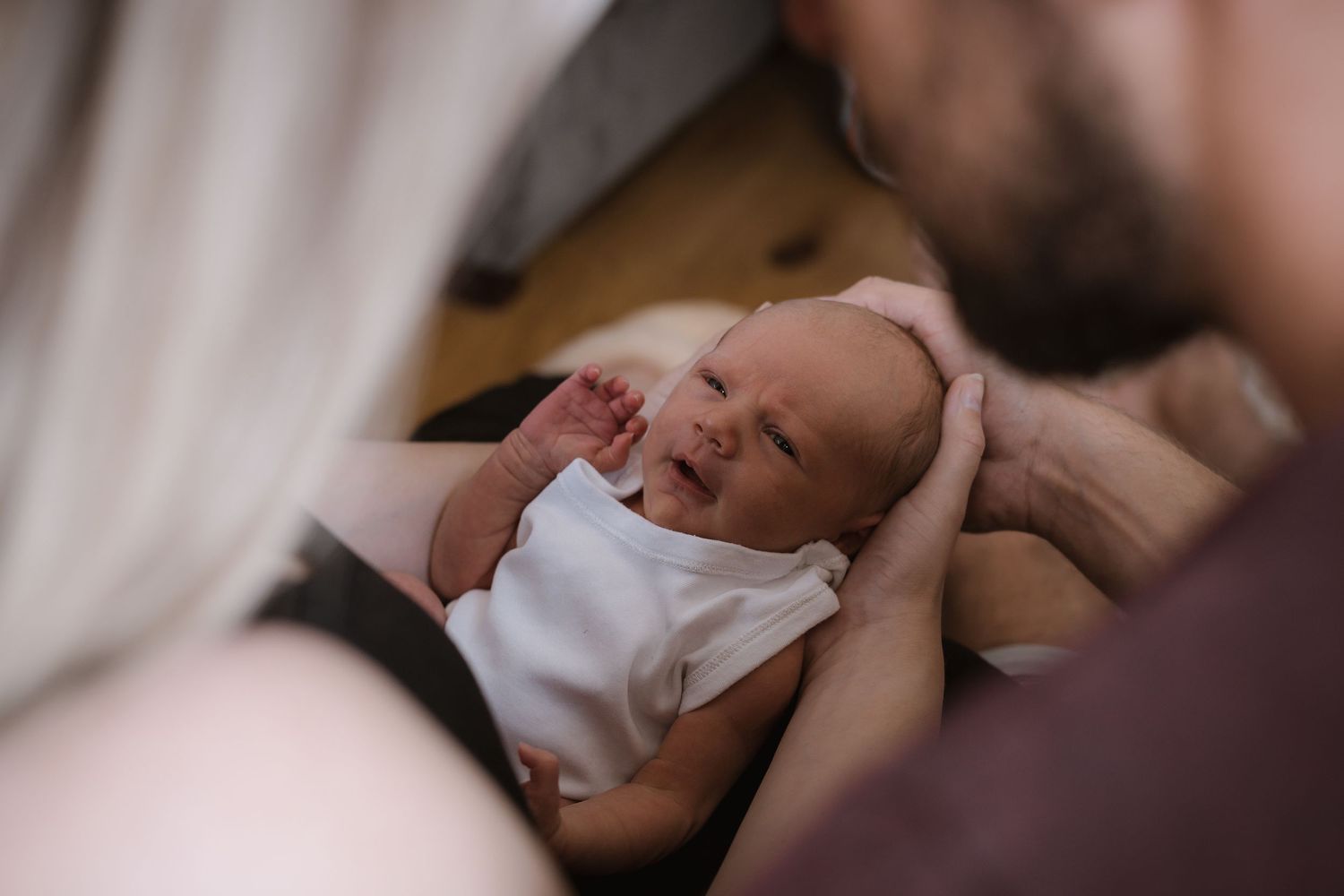 A sleeping newborn in white clothing being gently held by caregivers.