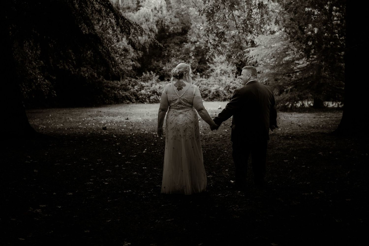 Silhouetted couple holds hands in a moody forest setting captured in dramatic black and white.