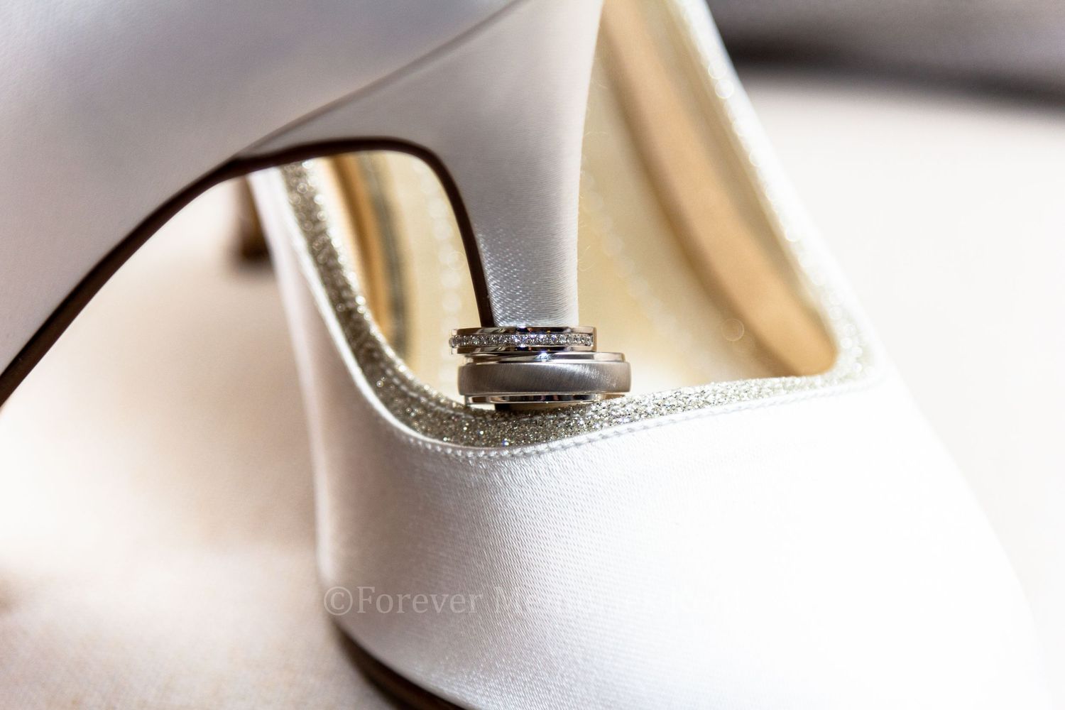 Wedding rings placed artistically on white bridal heels.