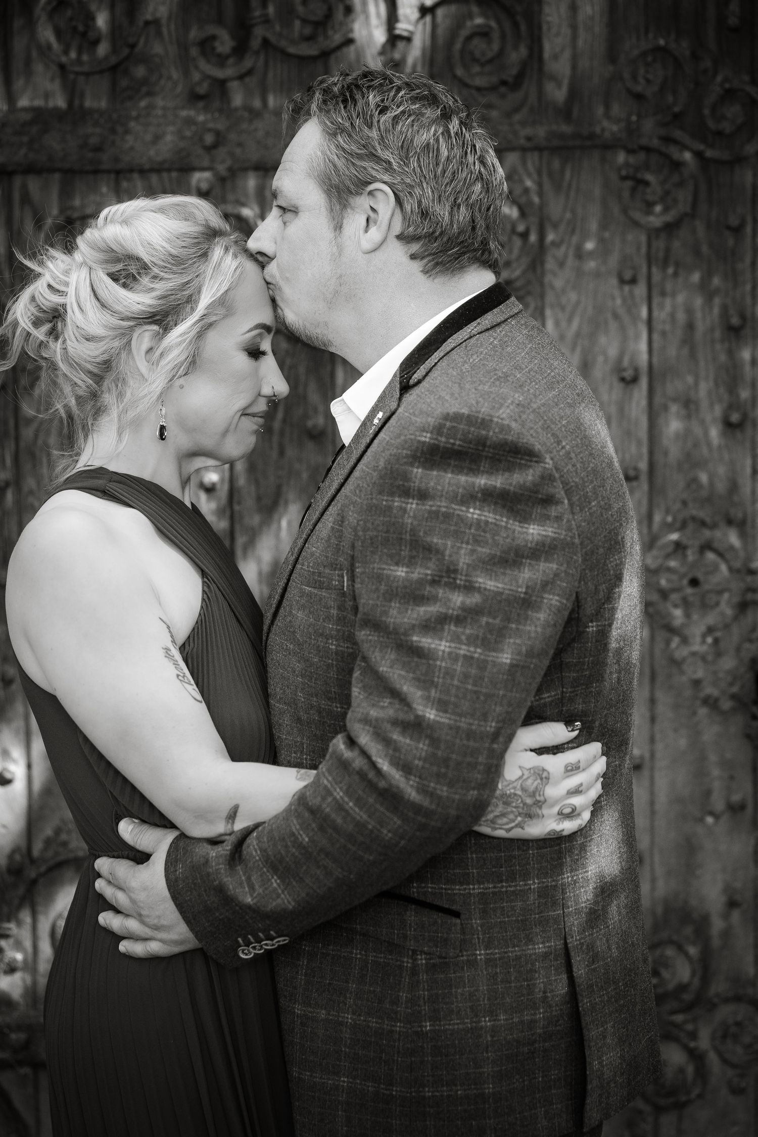 A romantic black and white portrait of a couple sharing an intimate moment against an ornate door background.