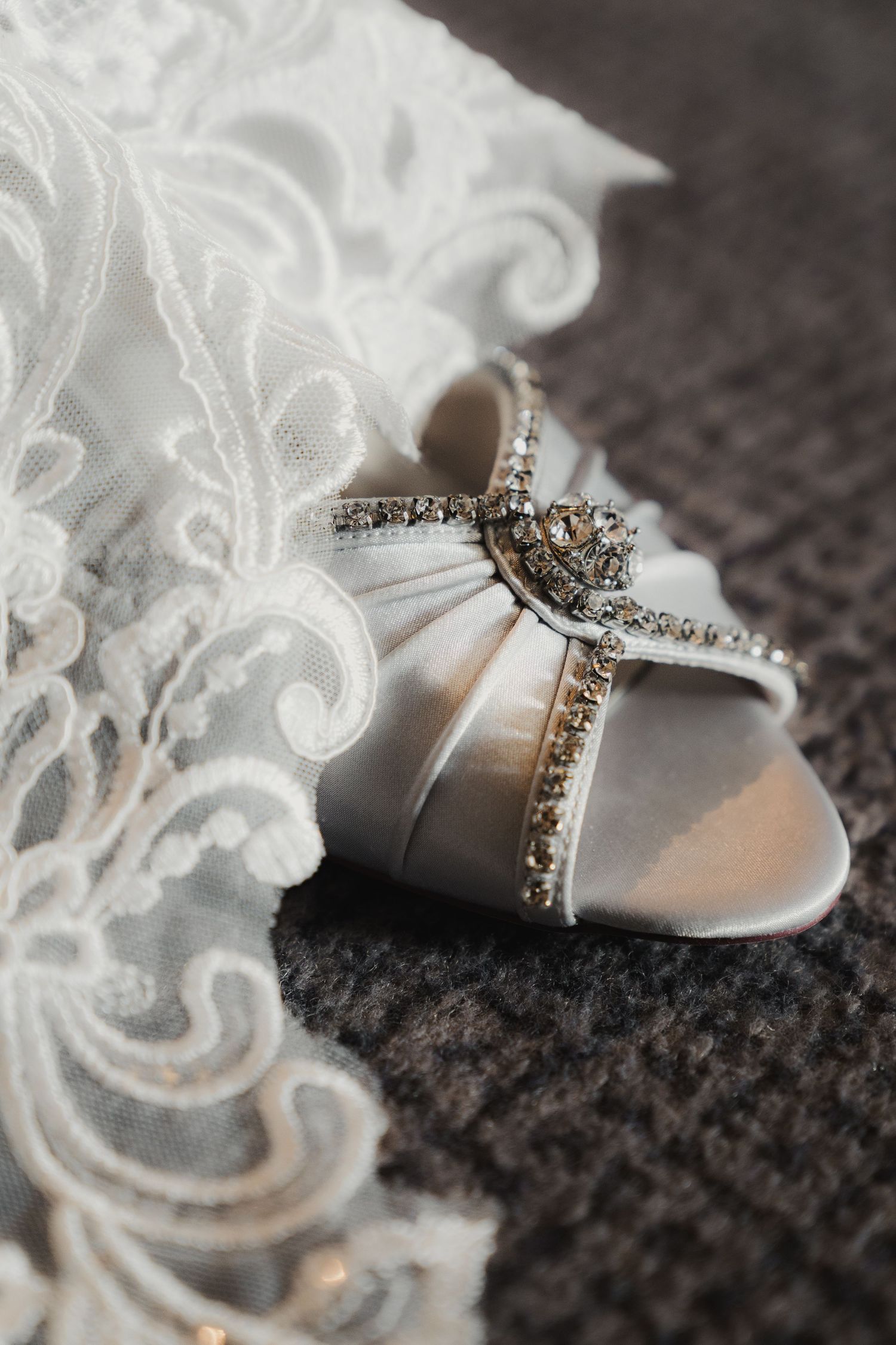 Close-up detail of white lace wedding dress fabric with crystal-embellished bridal shoe.