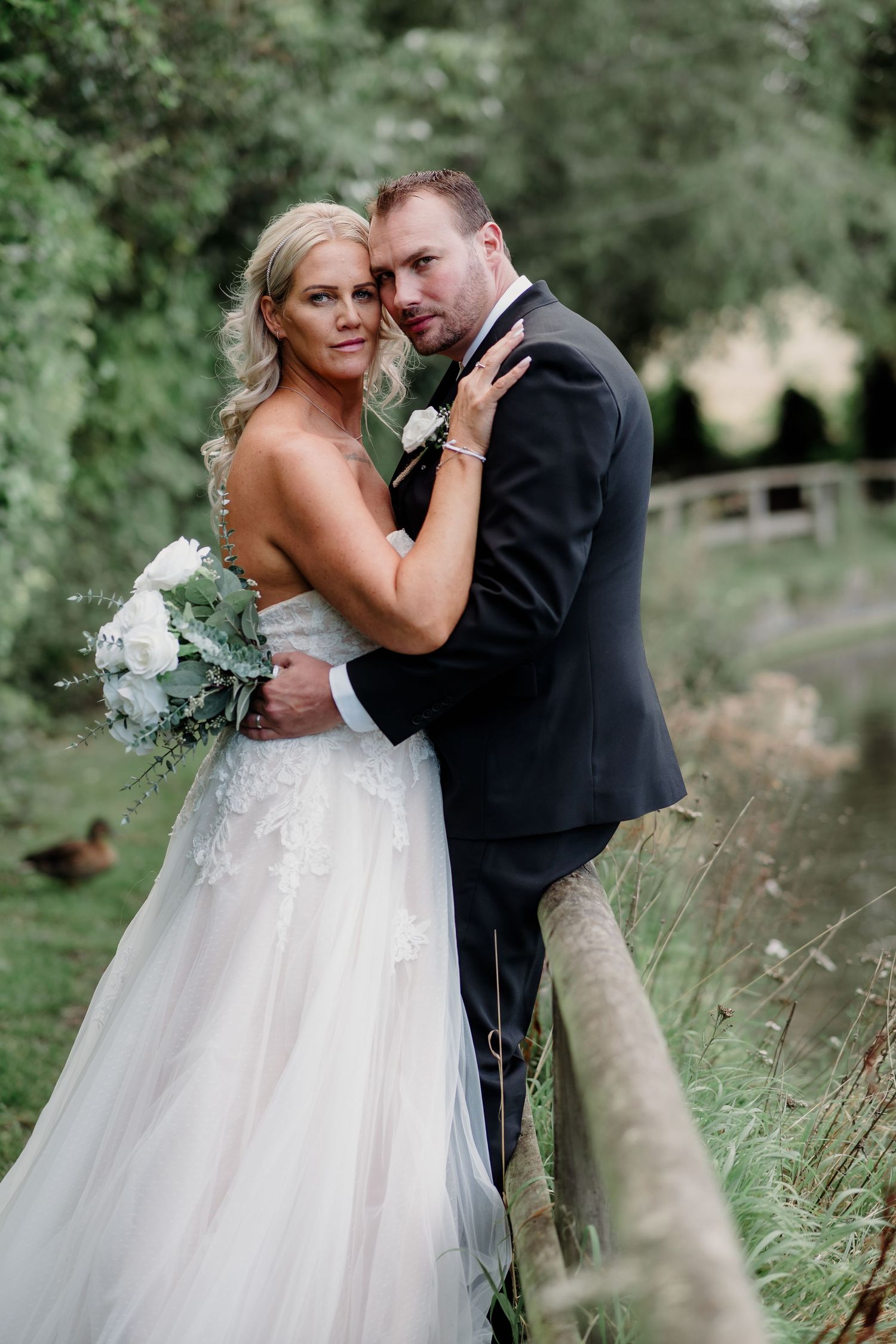 Romantic portrait of newlyweds embracing by wooden fence in garden setting.