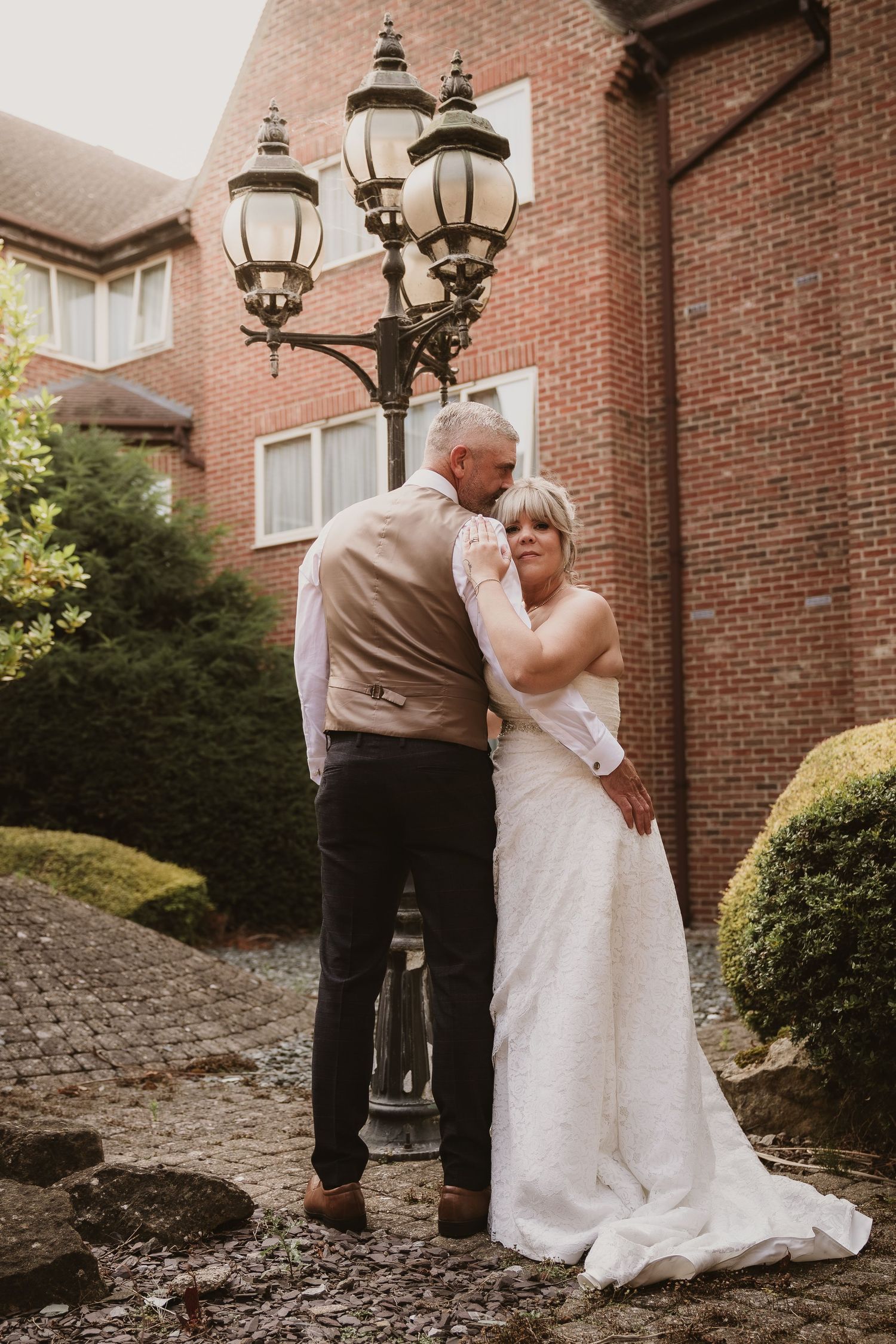 A romantic moment between a couple in wedding attire near a vintage lamp post and brick building.