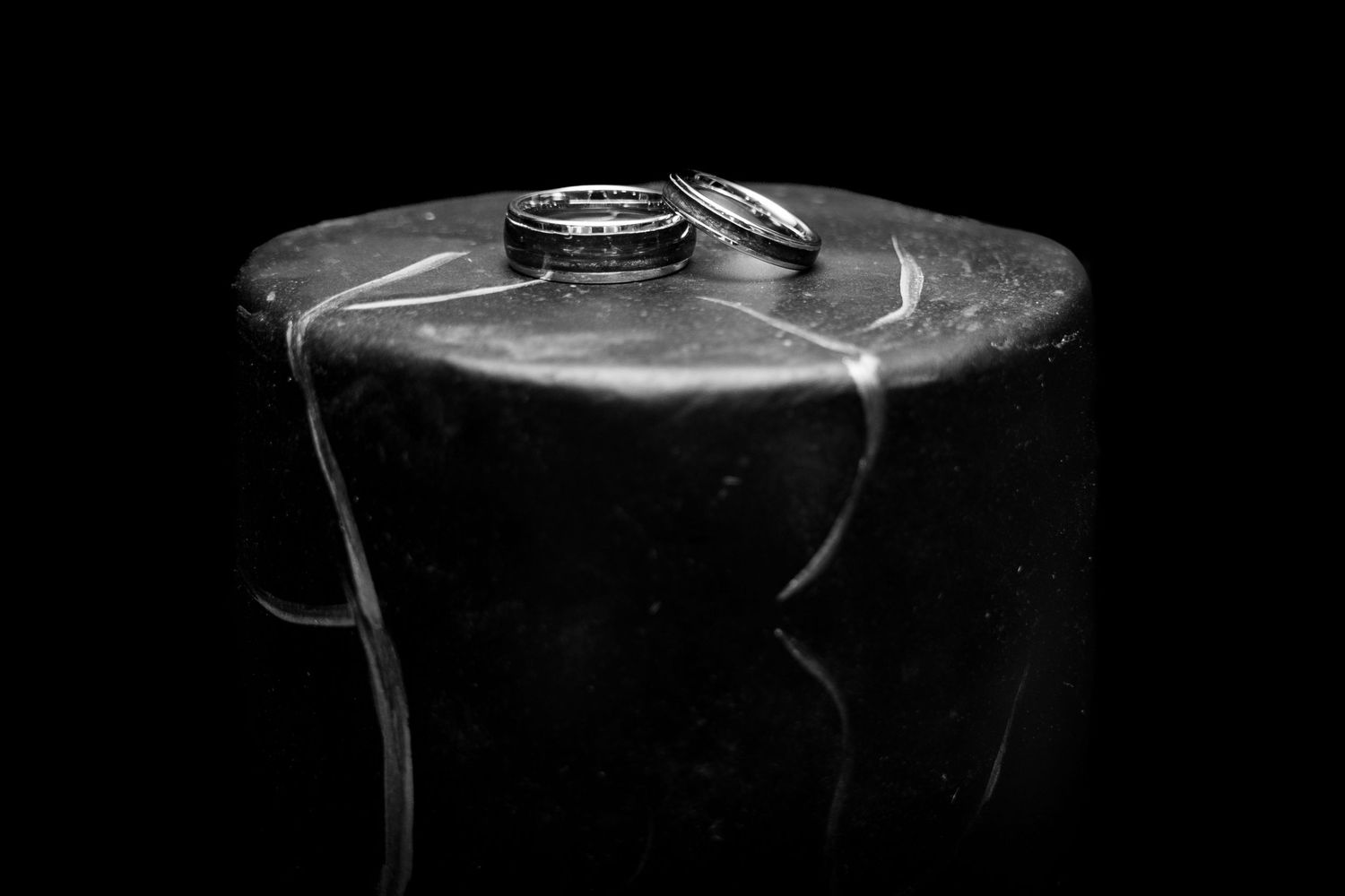Wedding rings displayed artistically on a dark surface in black and white.