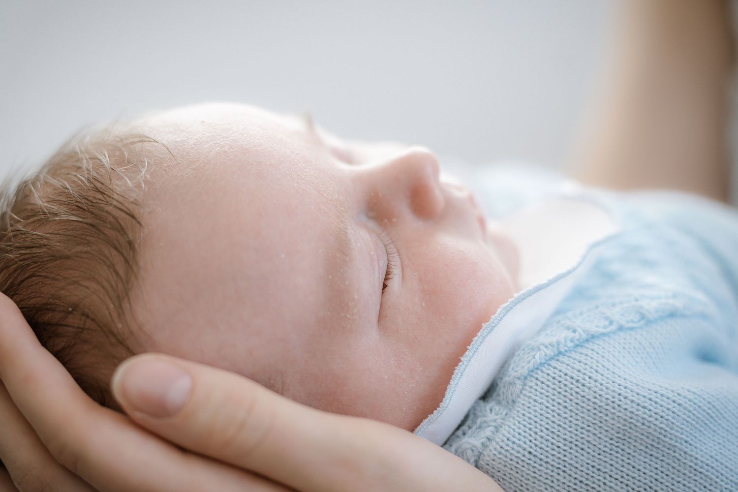Peaceful sleeping infant in blue sweater cradled by gentle hands.
