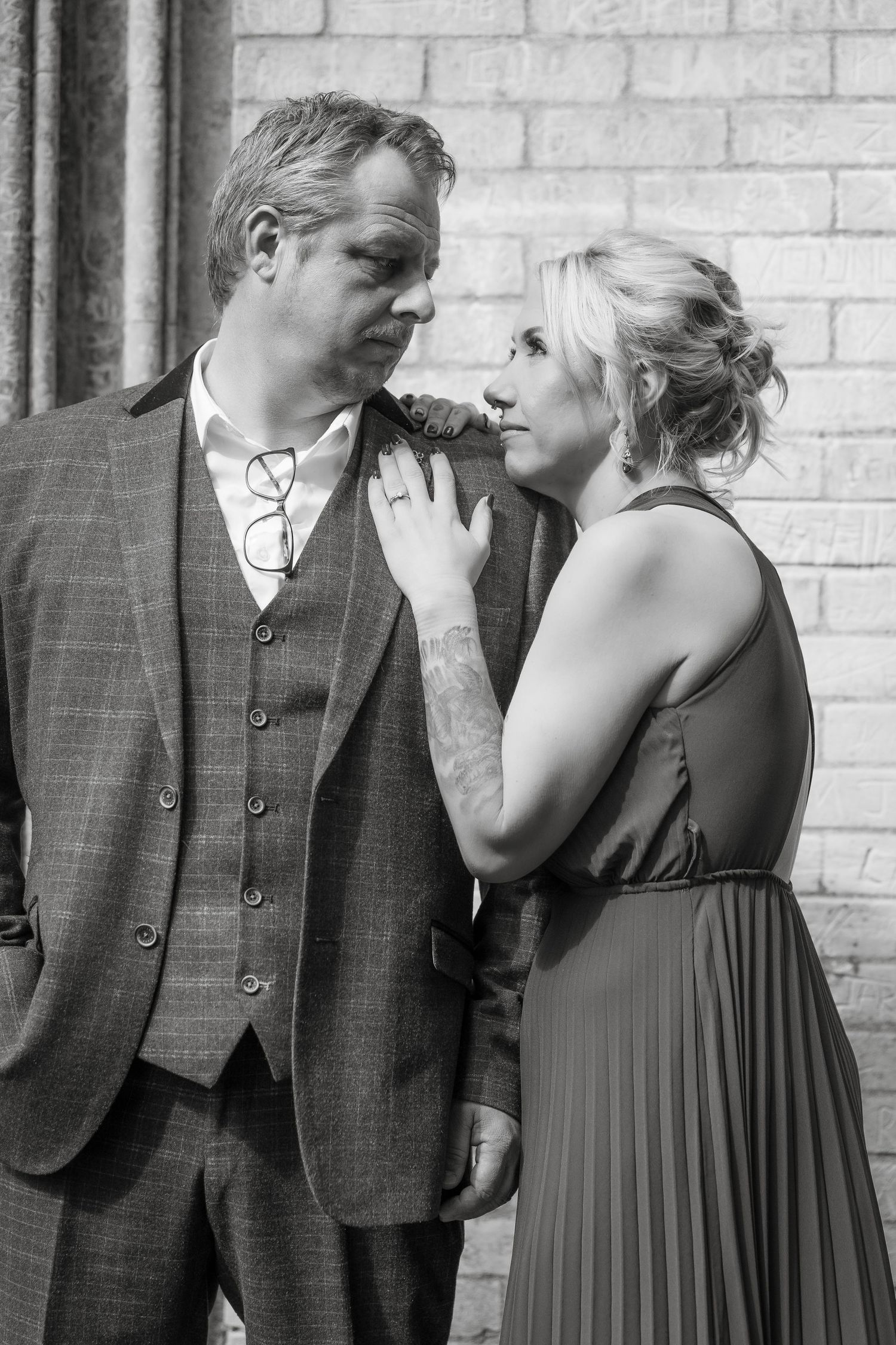 Black and white sequence showing a romantic couple in formal attire having an intimate moment against a brick wall.