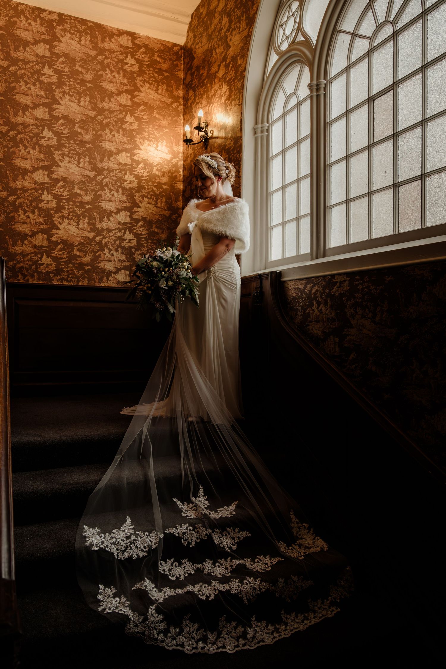 A dramatic bridal portrait with a long lace veil next to an arched window.