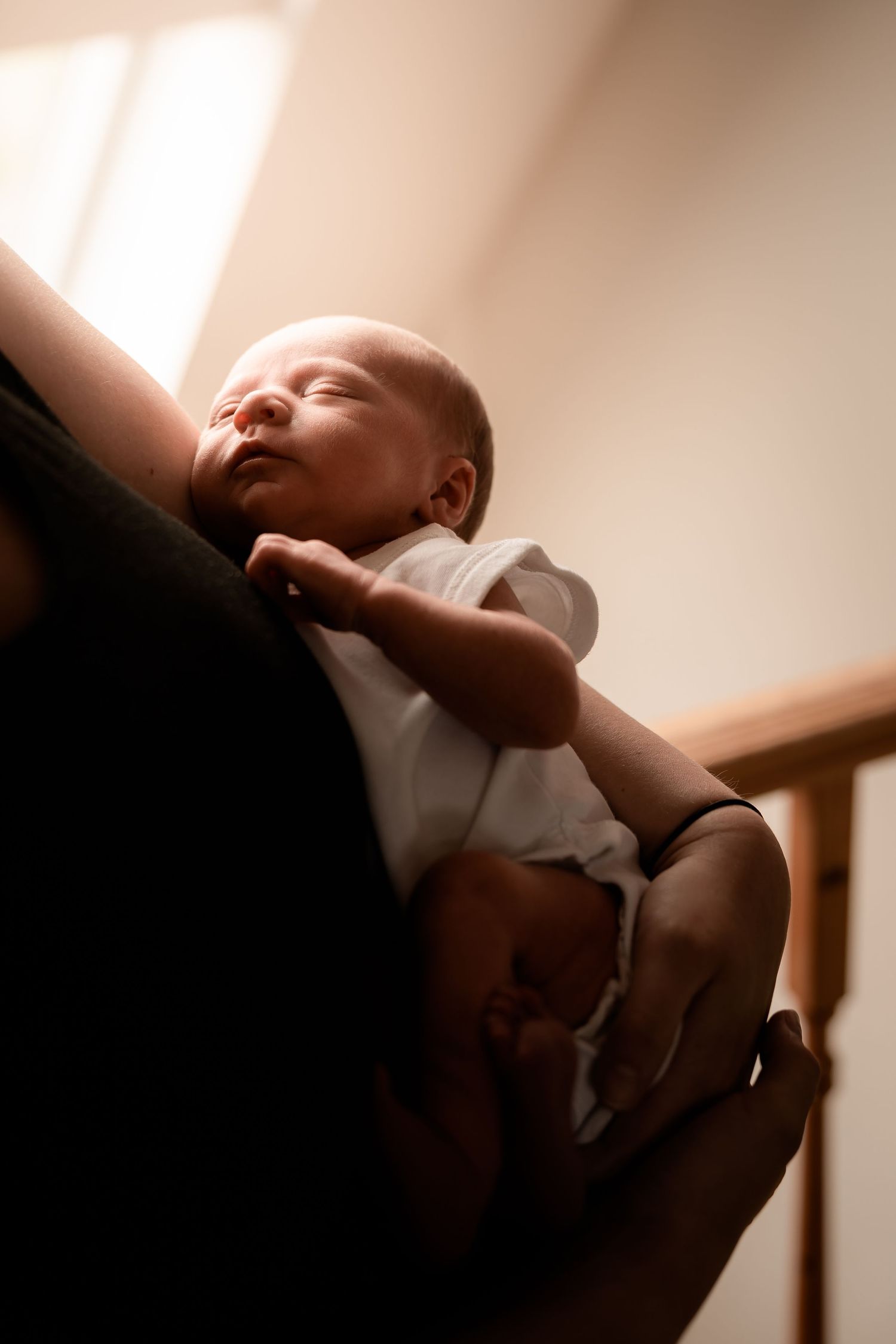 A sleeping infant in white clothing is cradled in gentle arms against a dark background.