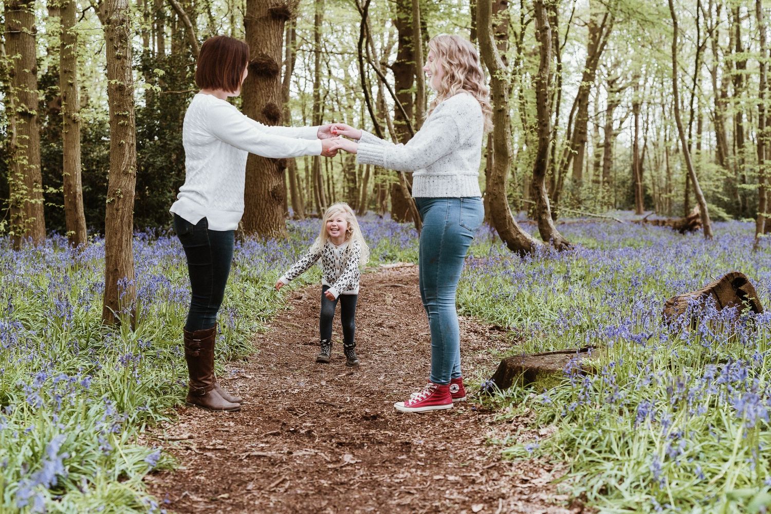 People walking through a scenic woodland path lined with blooming bluebells.