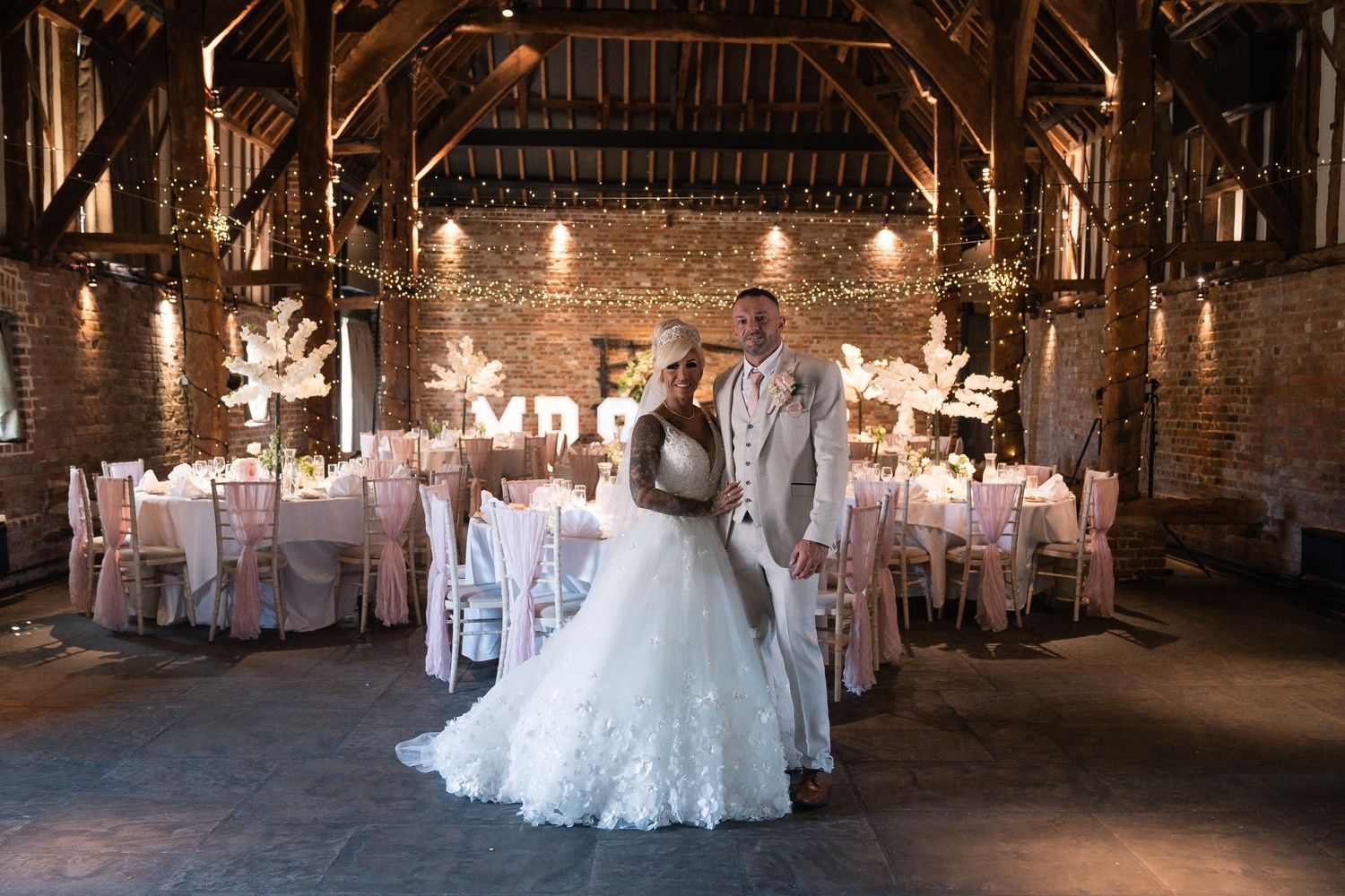 Wedding reception venue decorated with pink tables and string lights in a rustic barn setting.