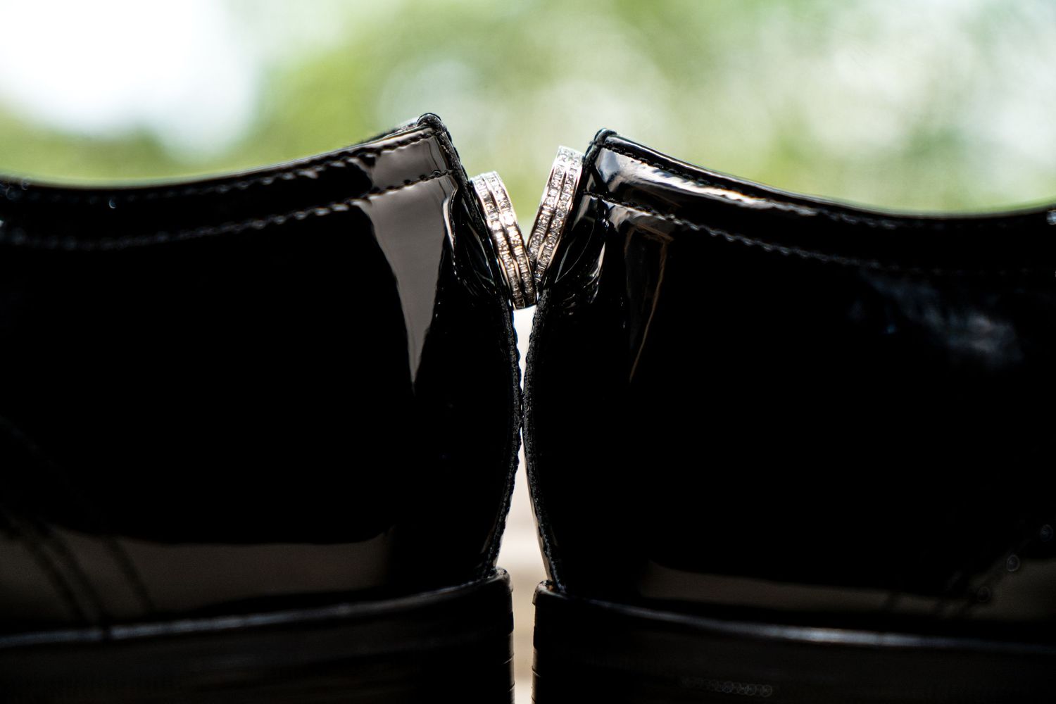 Close-up silhouette of two formal black dress shoes touching at the heels against a bright background.