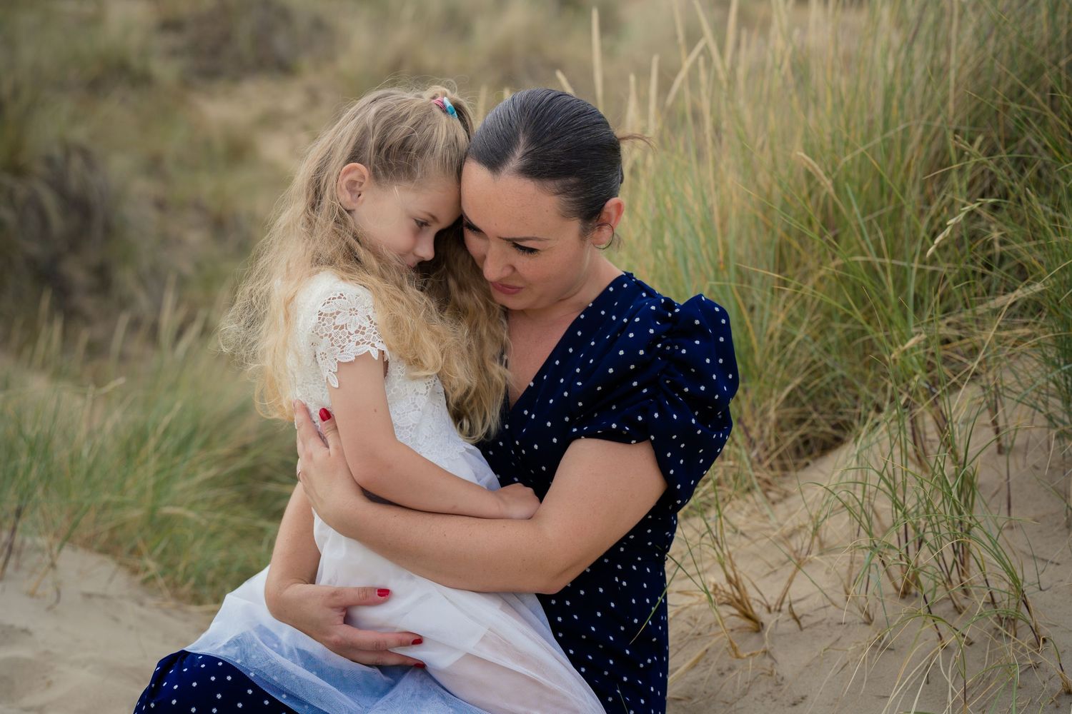 Intimate family moments captured on sandy beach with tall grass backdrop.