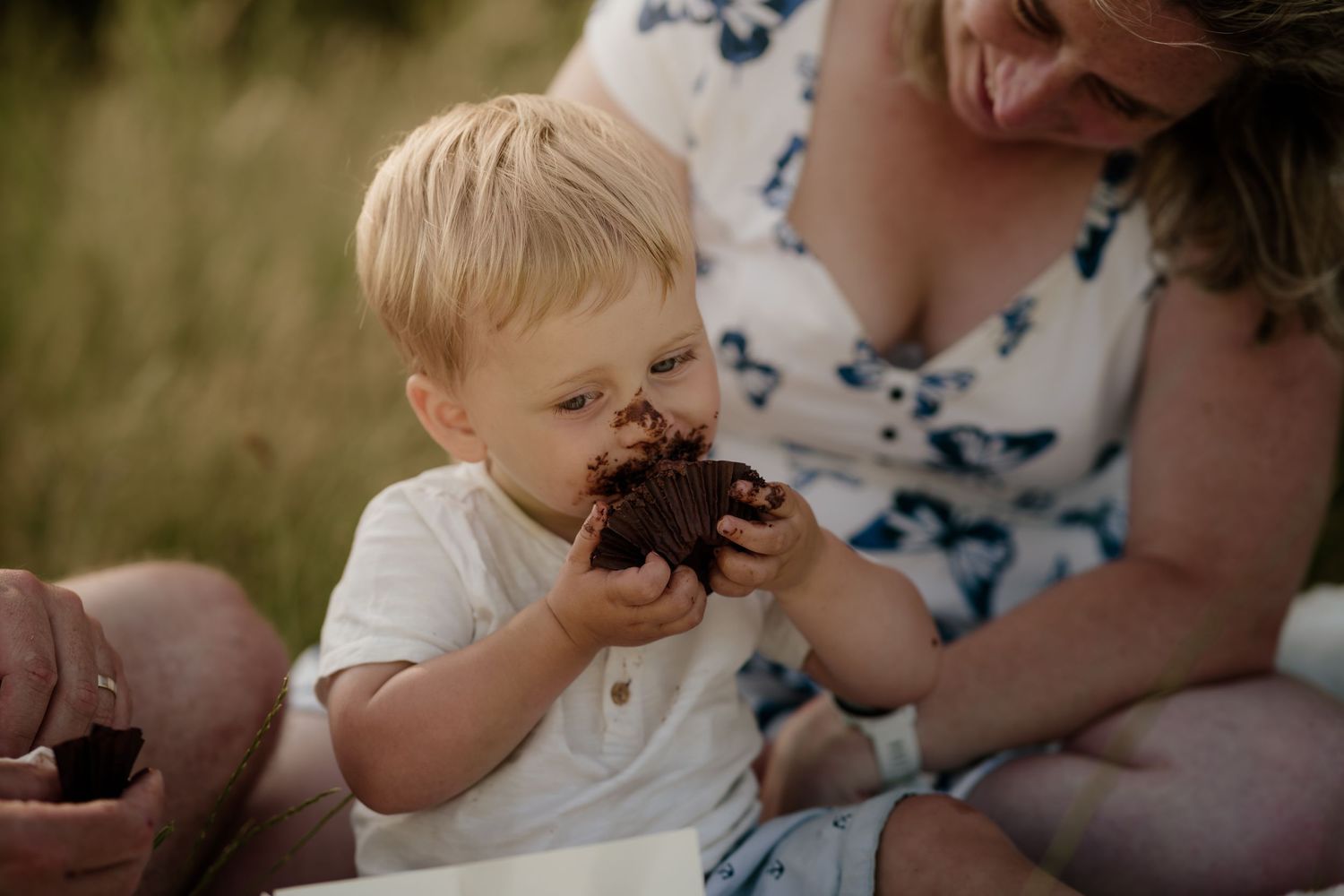 Child messily eating chocolate cake during outdoor picnic.