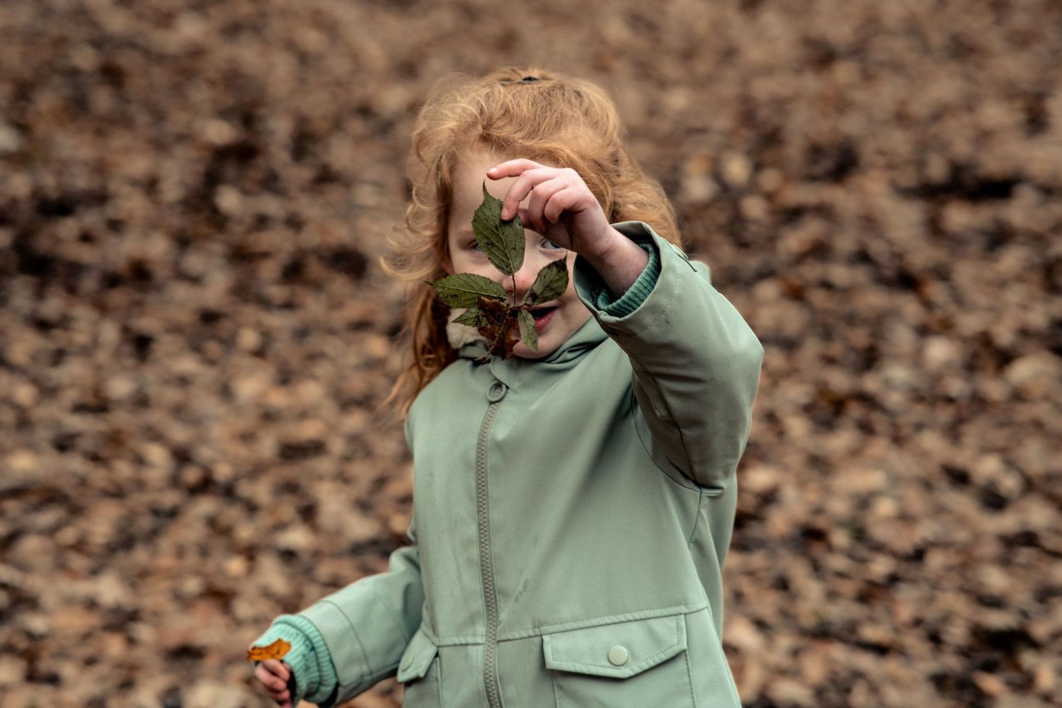 Child in mint green coat exploring outdoors while looking through imaginary binoculars.