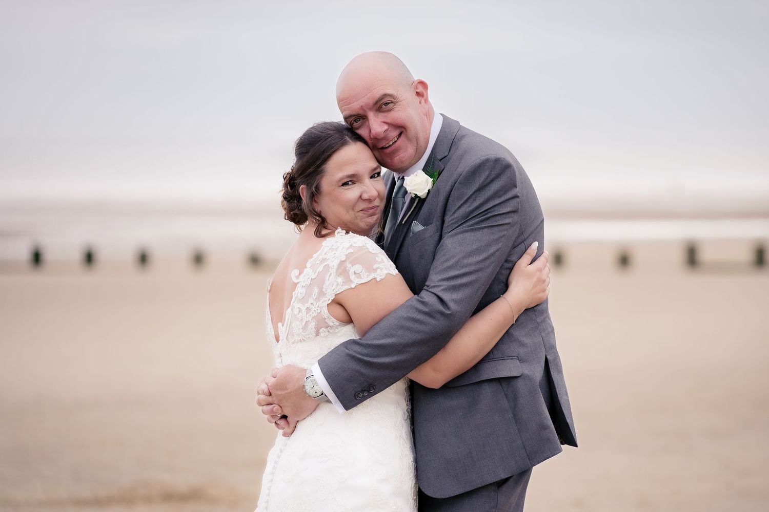 A tender embrace between newlyweds on a misty beach landscape.
