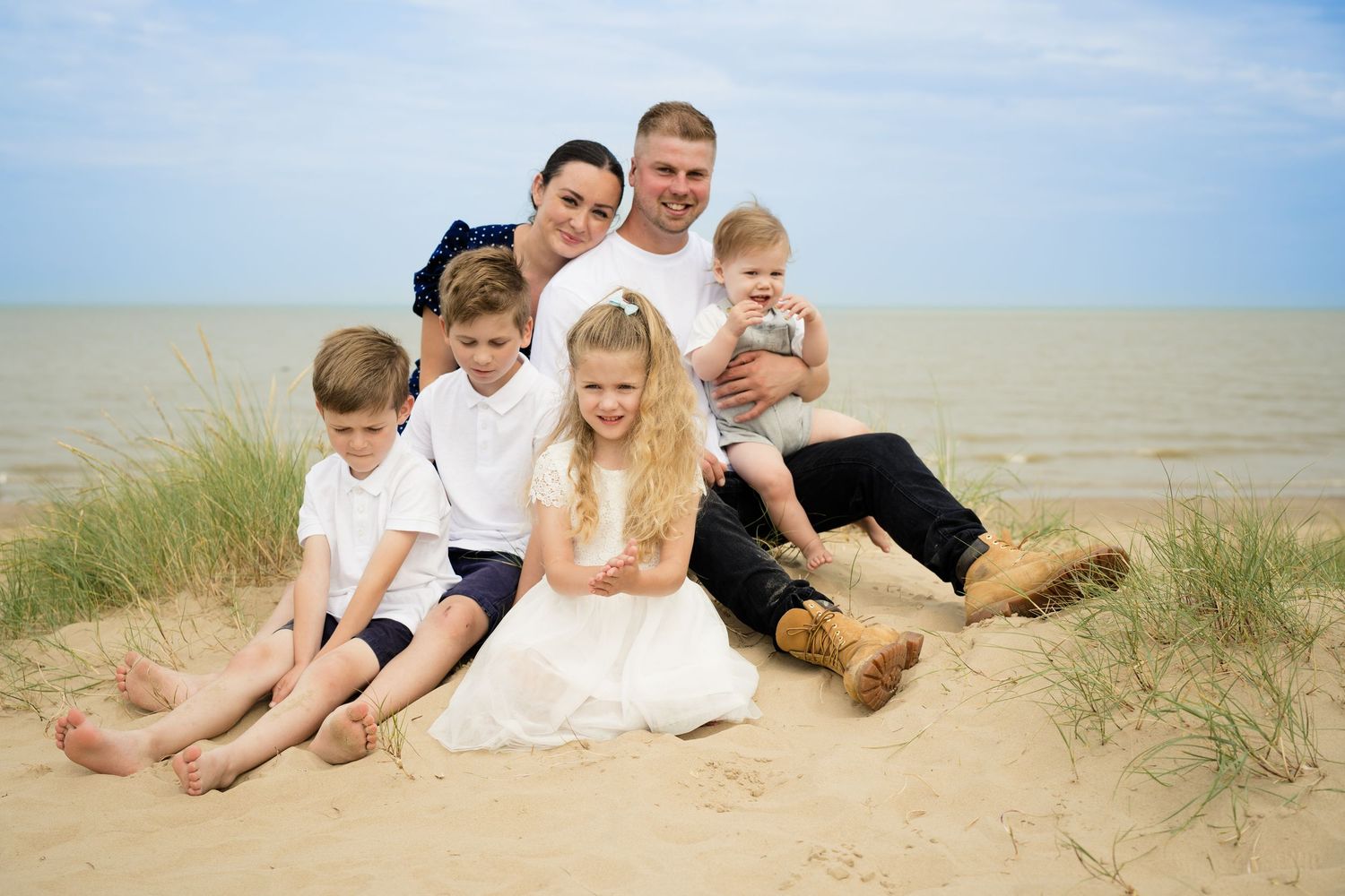 Happy family relaxing together on beach dunes during sunset.