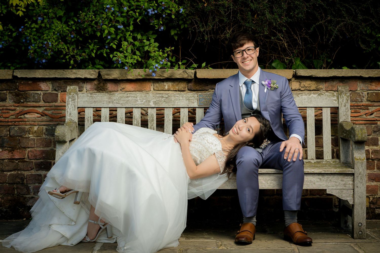 A couple rests on a garden bench during their wedding photoshoot.