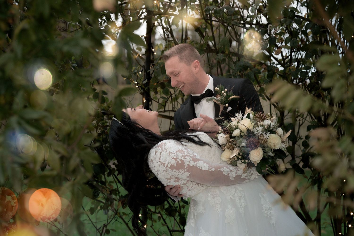 A romantic wedding dip pose surrounded by twinkling lights and greenery.