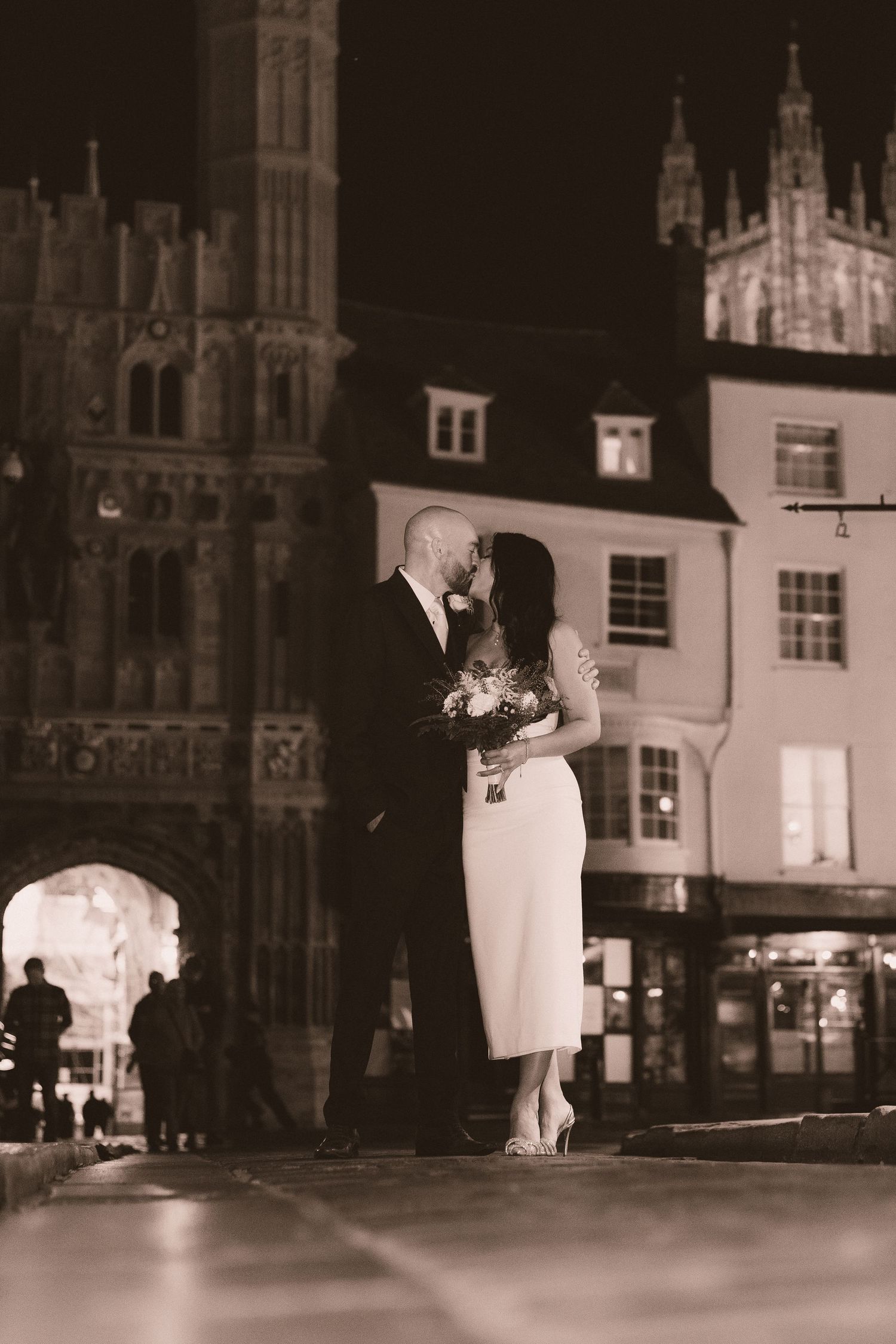 A romantic nighttime wedding portrait with gothic cathedral architecture illuminated in the background.