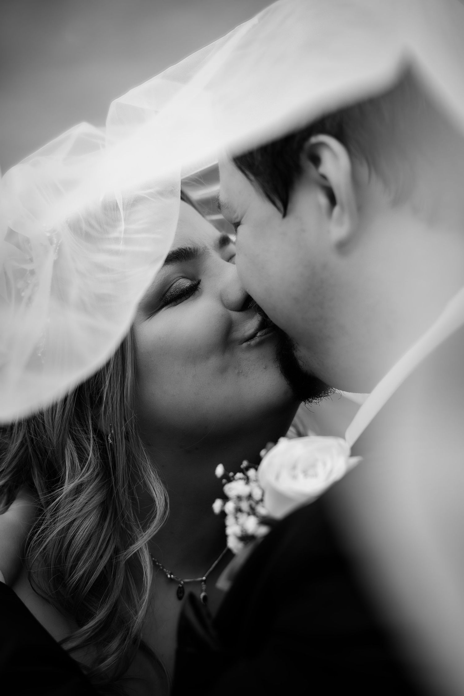 Romantic black and white wedding portrait of a couple sharing an intimate moment under a veil.