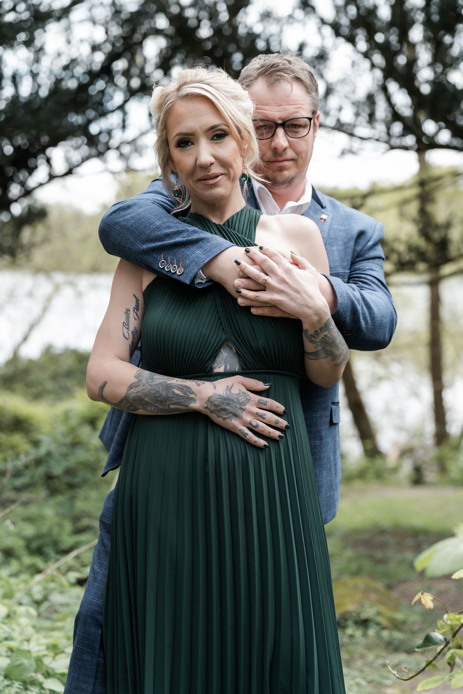A romantic outdoor couple portrait shows an embrace with the woman in a green pleated dress and the man in a blue suit.
