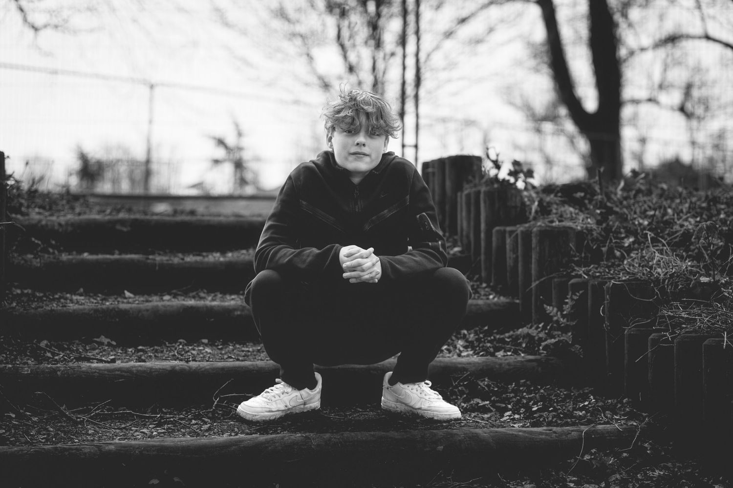 Black and white portrait of someone crouching on dark stone steps outdoors.