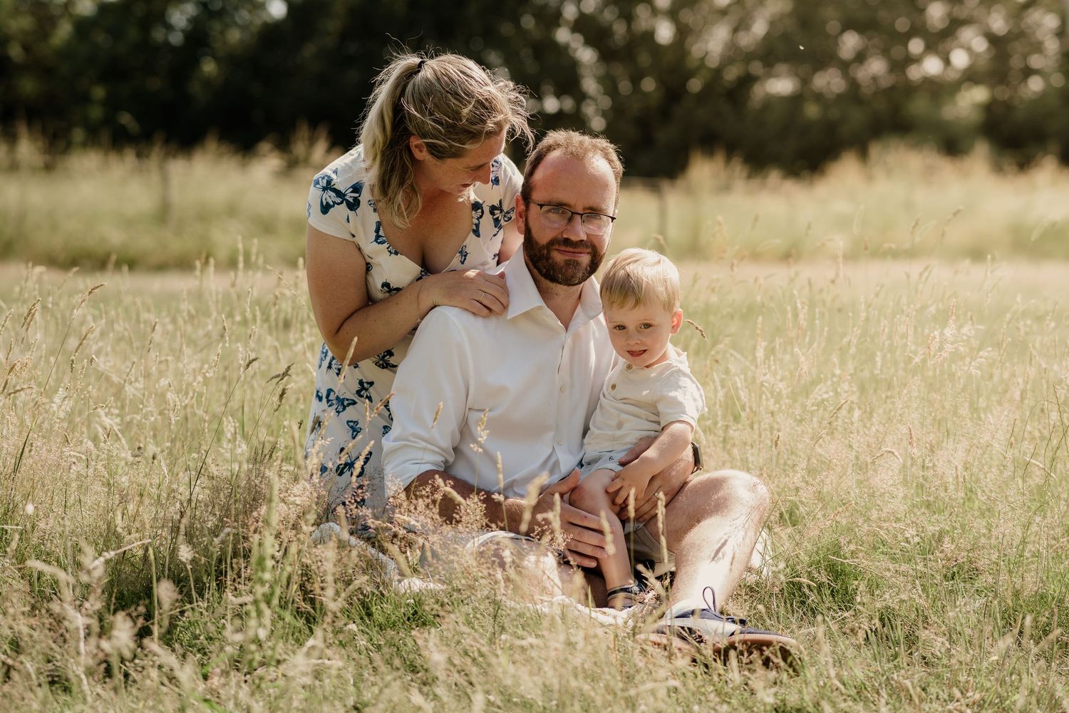 Family sitting together in a sunny meadow with tall golden grass.
