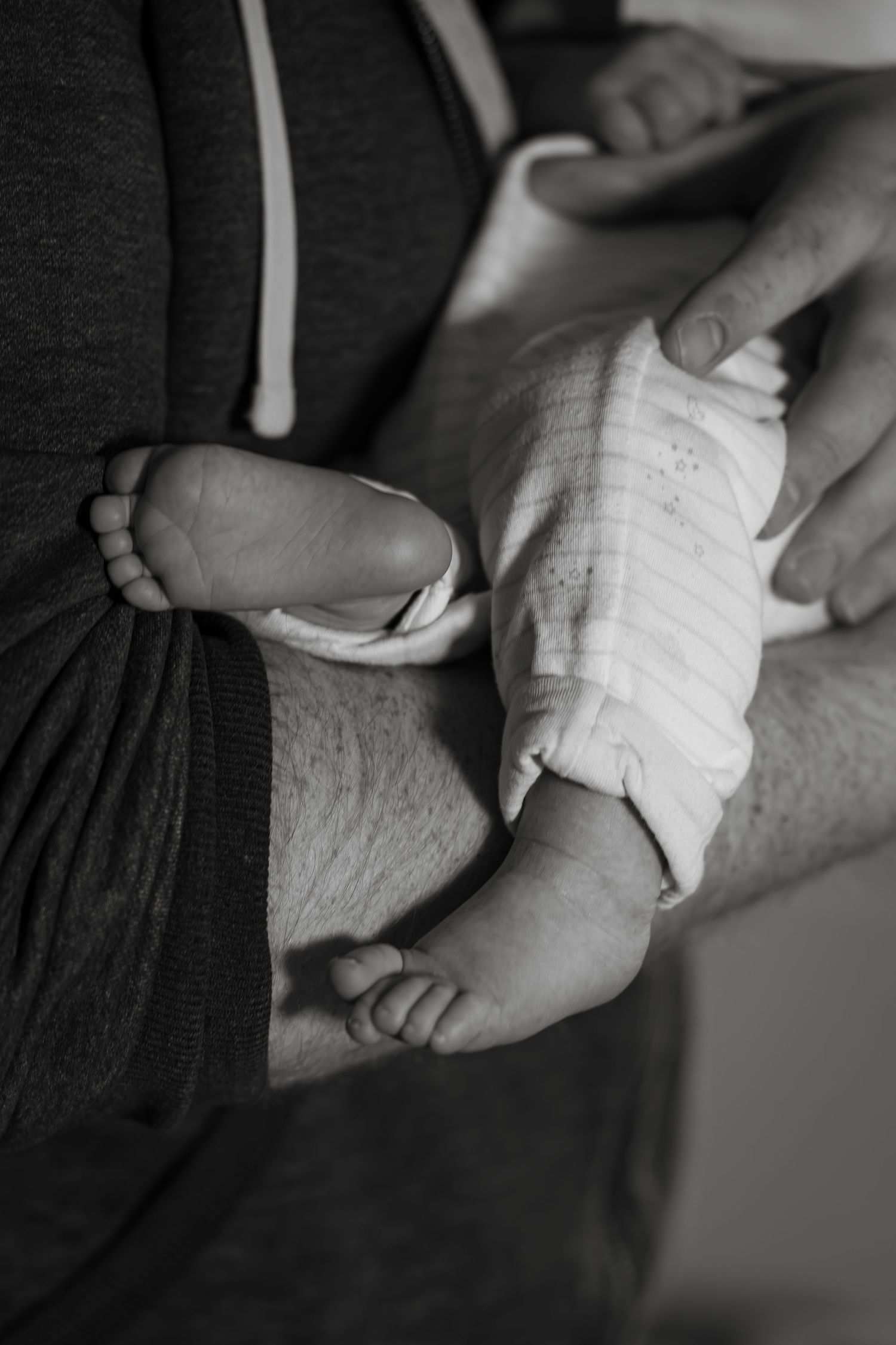 Black and white image of bandaged newborn feet being held by caring hands.