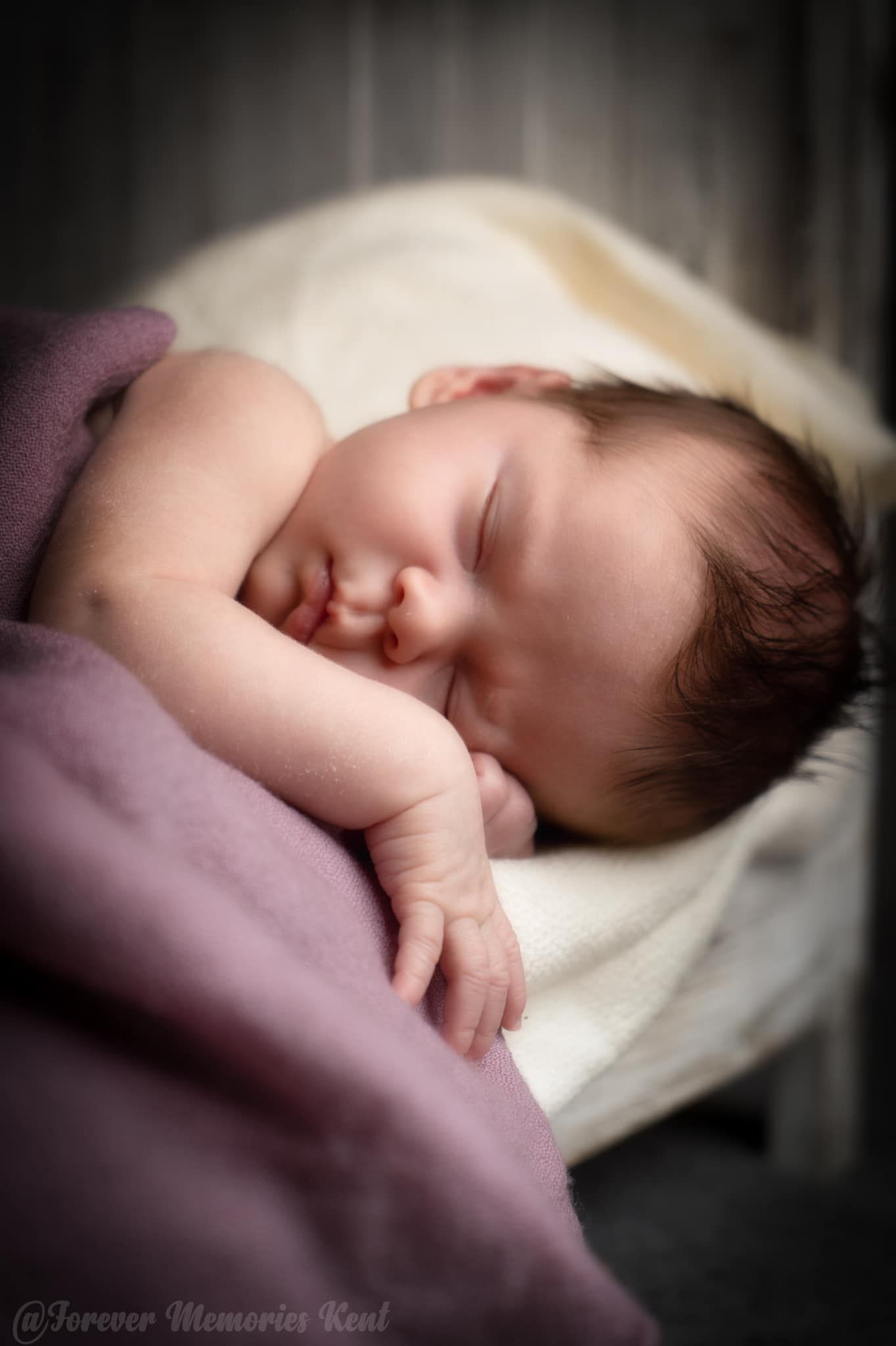 Peaceful sleeping newborn wrapped in purple and white blankets.