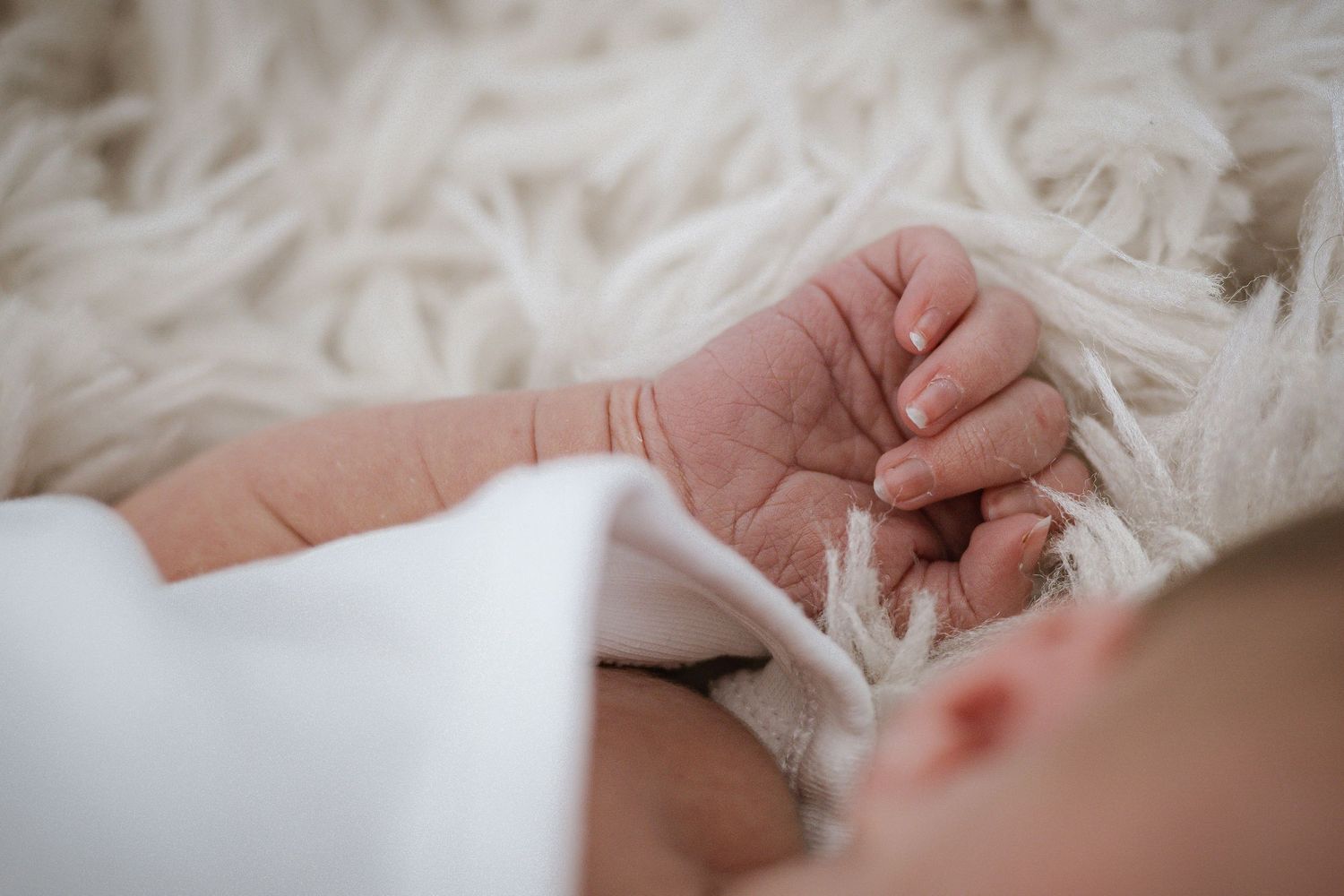 Close-up of a baby's delicate hand resting on white fluffy fabric.