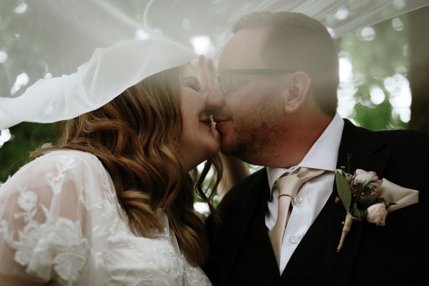 A romantic wedding moment captured with sunlight filtering through trees.